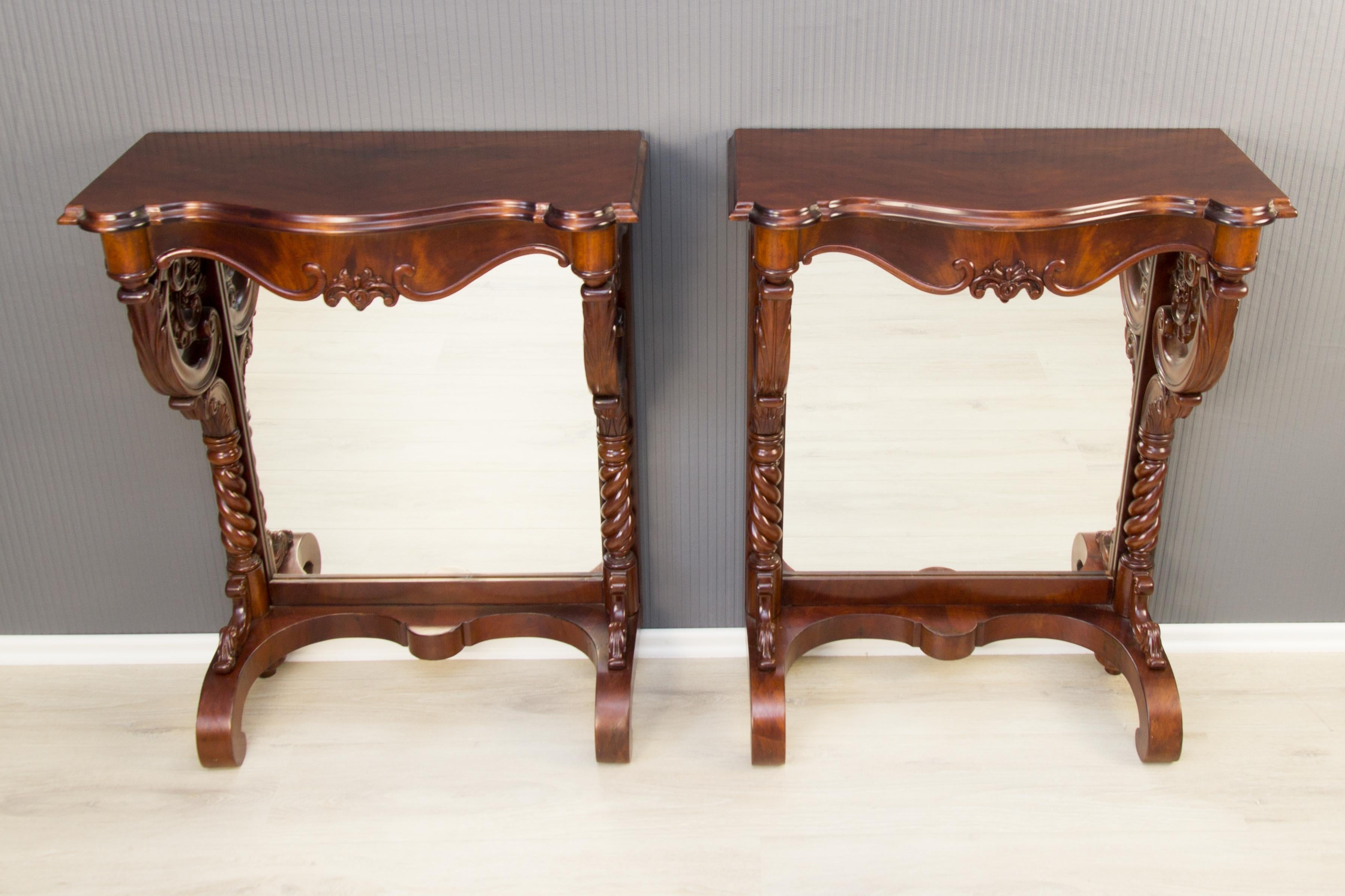 Pair of Regency style walnut wall console tables from circa 1860 France are raised on carved scrolling supports with mirrored back panels. The legs and front of the consoles are decorated with carved floral and acanthus leaf motifs.
The mirror backs