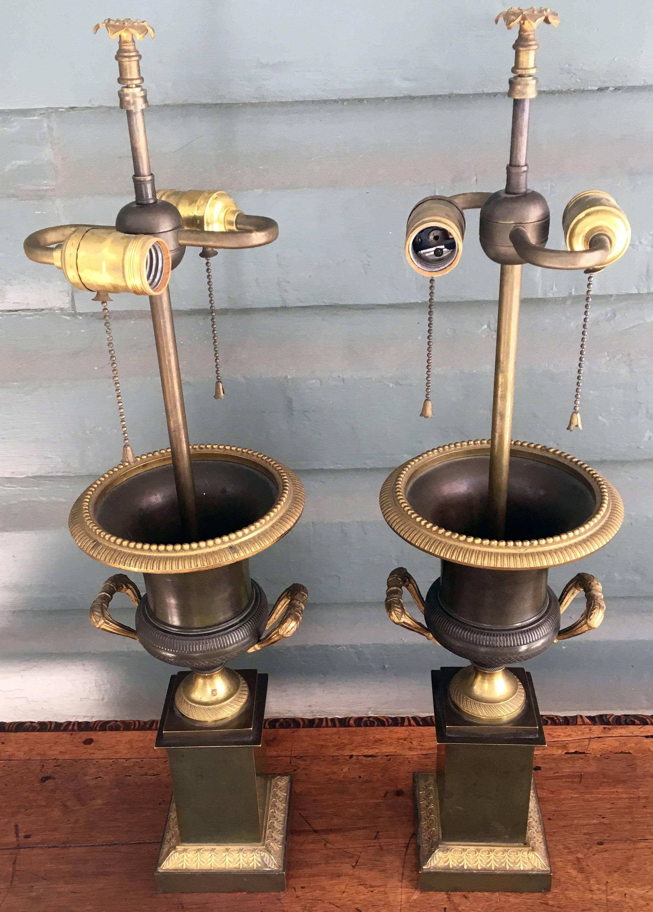 Patinated Bronze and doré bronze French urns, circa 1810, transformed into lamps. The urns having molded and beaded rims with cast bronze handles supported on plinth bases.
Measure: -25.5