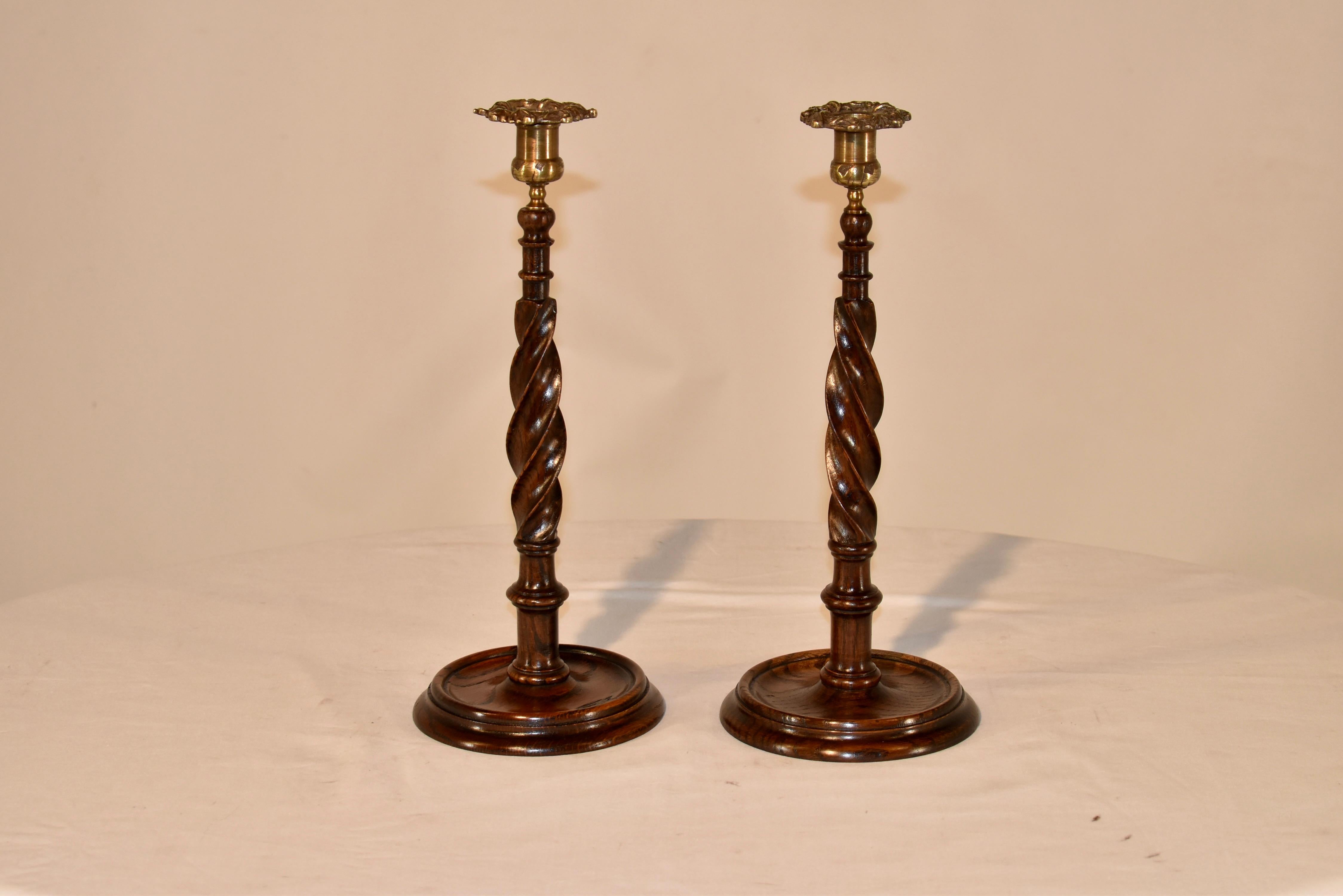 Pair of 19th century oak candlesticks from England. The candle cups are beautifully hand cast from brass and are reminiscent of florals, perched on top of hand turned ribbon twist stems. The edges are so sharp and crisp, they are delightful in