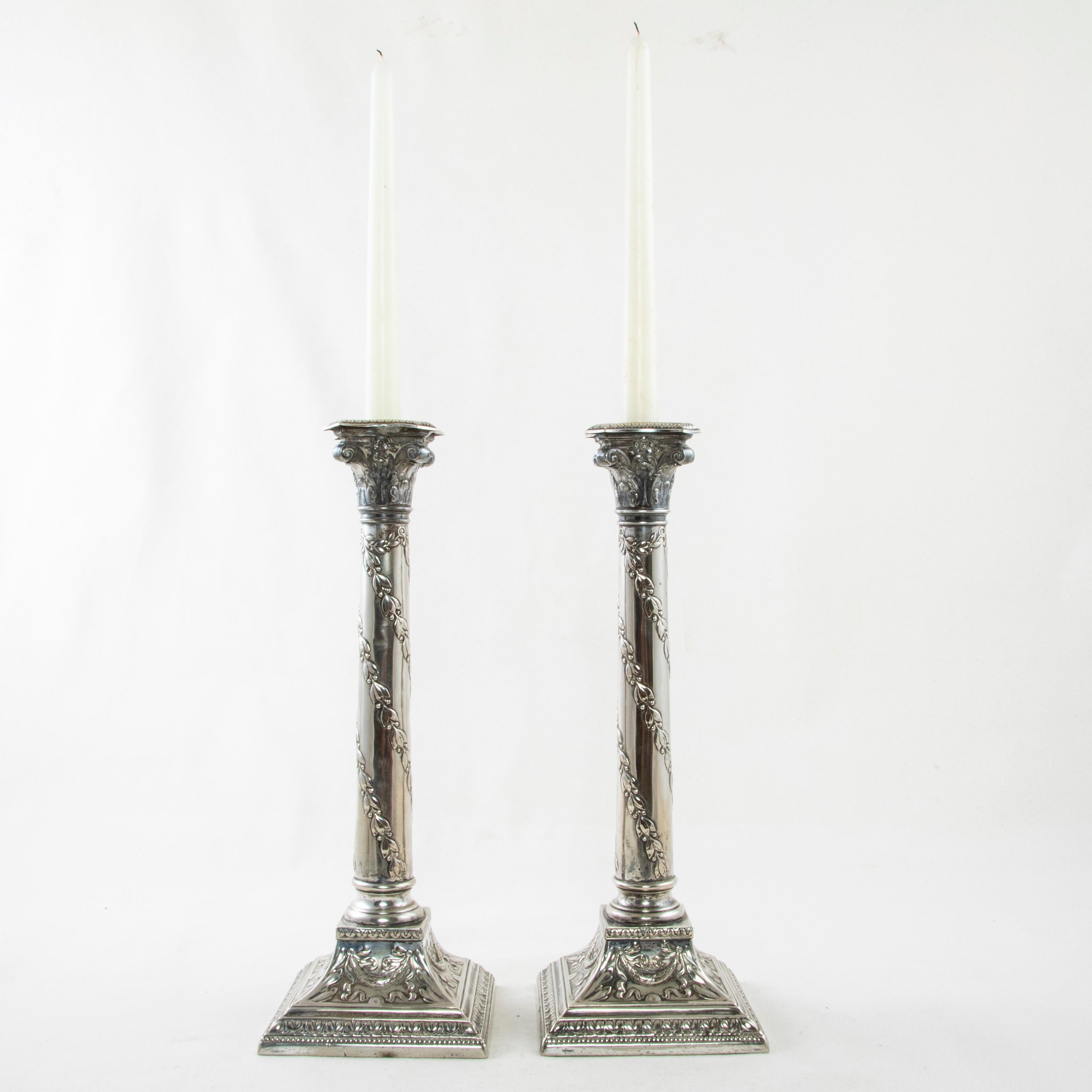 This pair of late 19th century 13 inch tall silver plate candlesticks from Romania features Classic Louis XVI motifs. Each candlestick takes the form of a column with a Corinthian capital. A spiraling laurel garland details the central pillar. Its