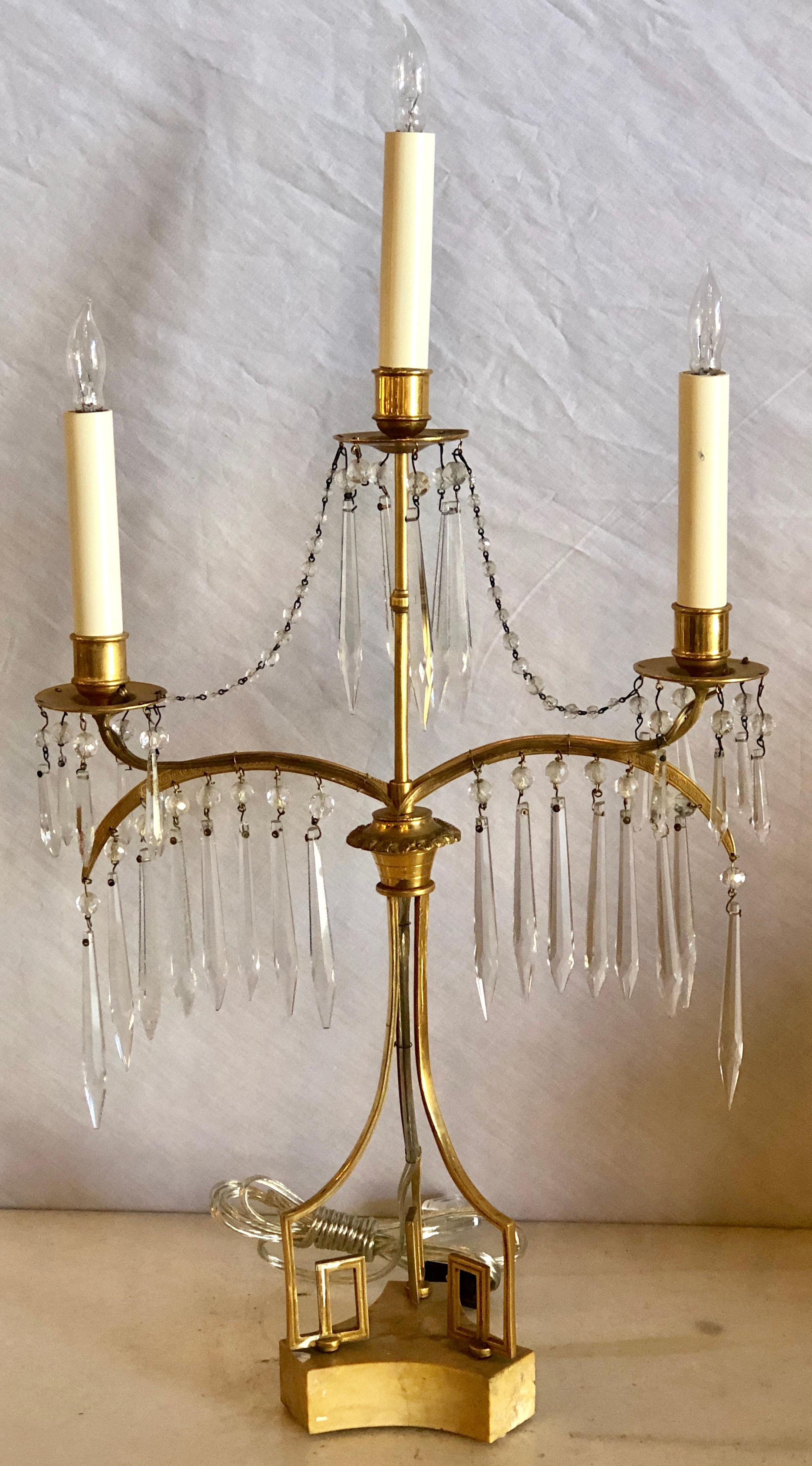 Pair of 19th century Russian neoclassical gilded bronze table lamps. These sleek and stylish table lamps are done in the candelabra style having three lights with finely cut crystals handing from the slender finely cast bodies supported by