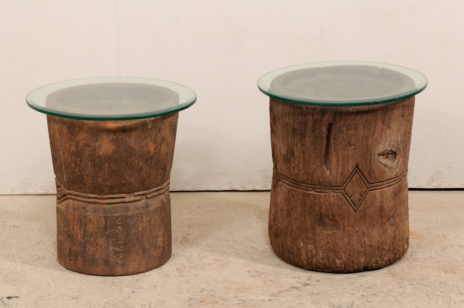 This is a beautiful pair of 19th century carved wooden mortar with glass top side tables. These unique pair of tables has been fashioned out of a pair of 19th century hand-carved wooden mortars from South Indian (Kerala), which have been topped with