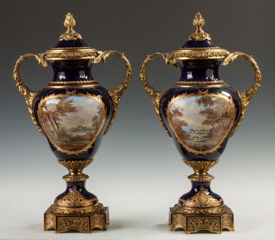 Pair of 19th century Sèvres style cobalt blue painted porcelain urns.
A fine pair of Sèvres style porcelain cobalt blue covered urns with courting couples and landscapes.

Origin: French
Date: 19th century 
Dimension: 25 in x 14 in.