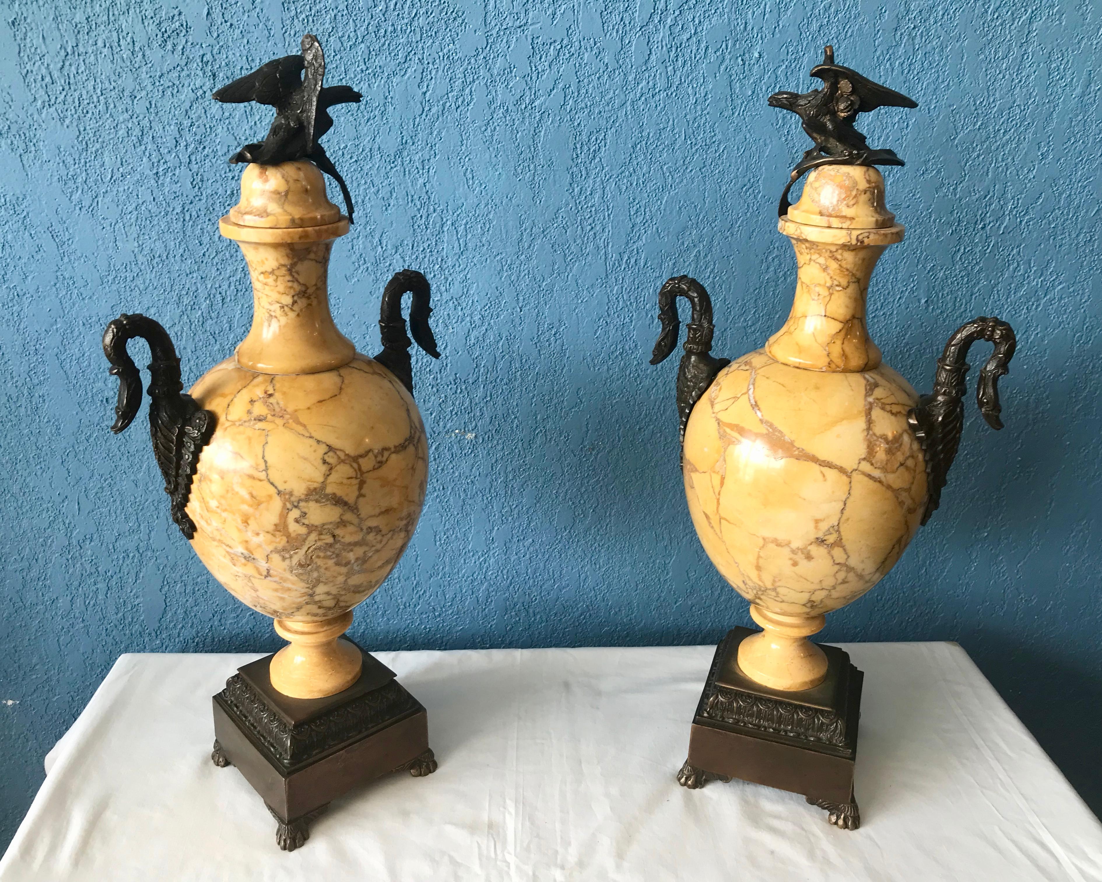 The impressive urns are appointed with swan motif handles and fitted with eagle finials.
They are raised upon bronze bases that terminate with paw feet.