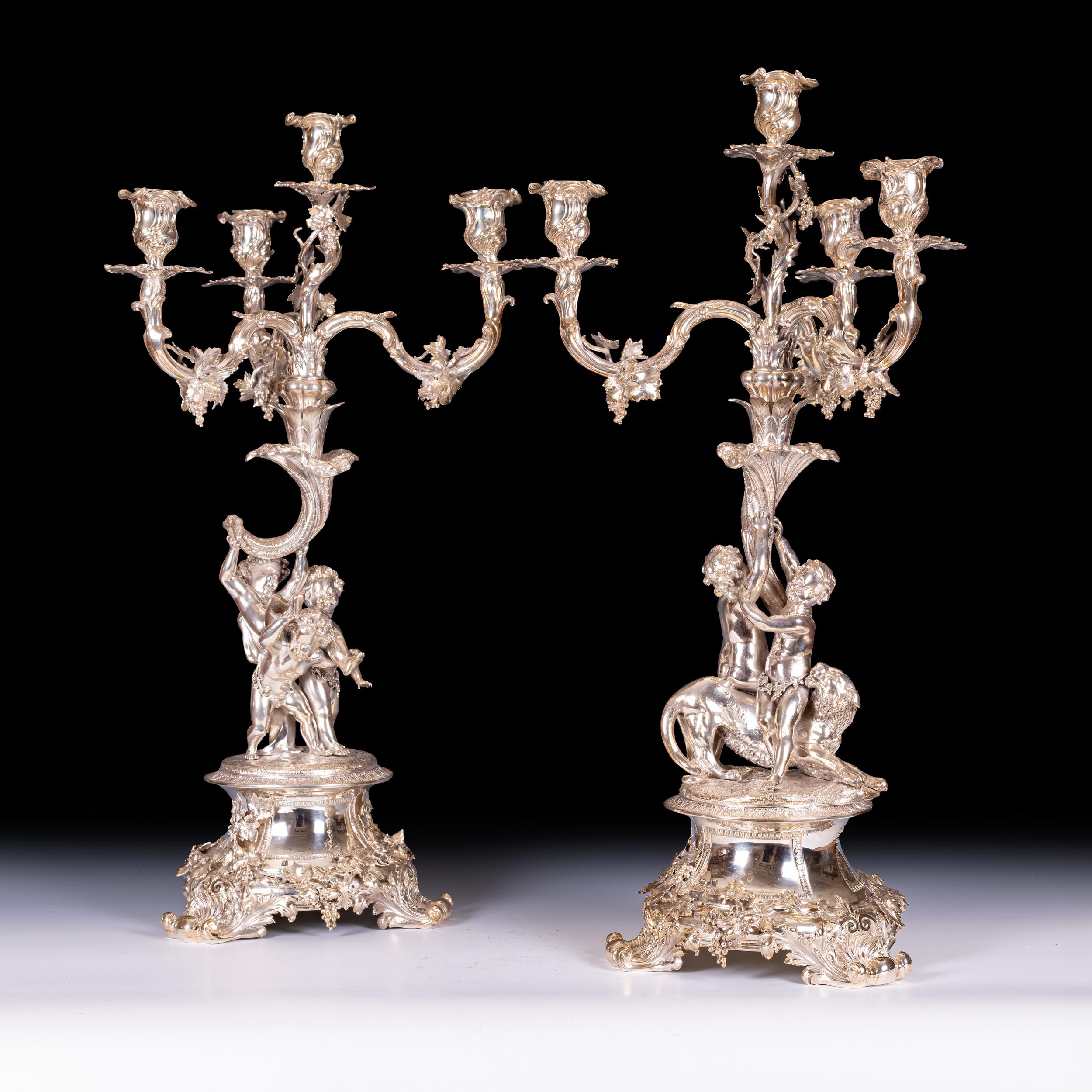 Un'importante coppia di candelabri in argento a quattro rami di Hunt e Roskill, di forma naturalistica con le quattro apparizioni su rami di vite fruttiferi sollevati su puttini con un leone raffigurato mentre si diverte su una piattaforma sopra un