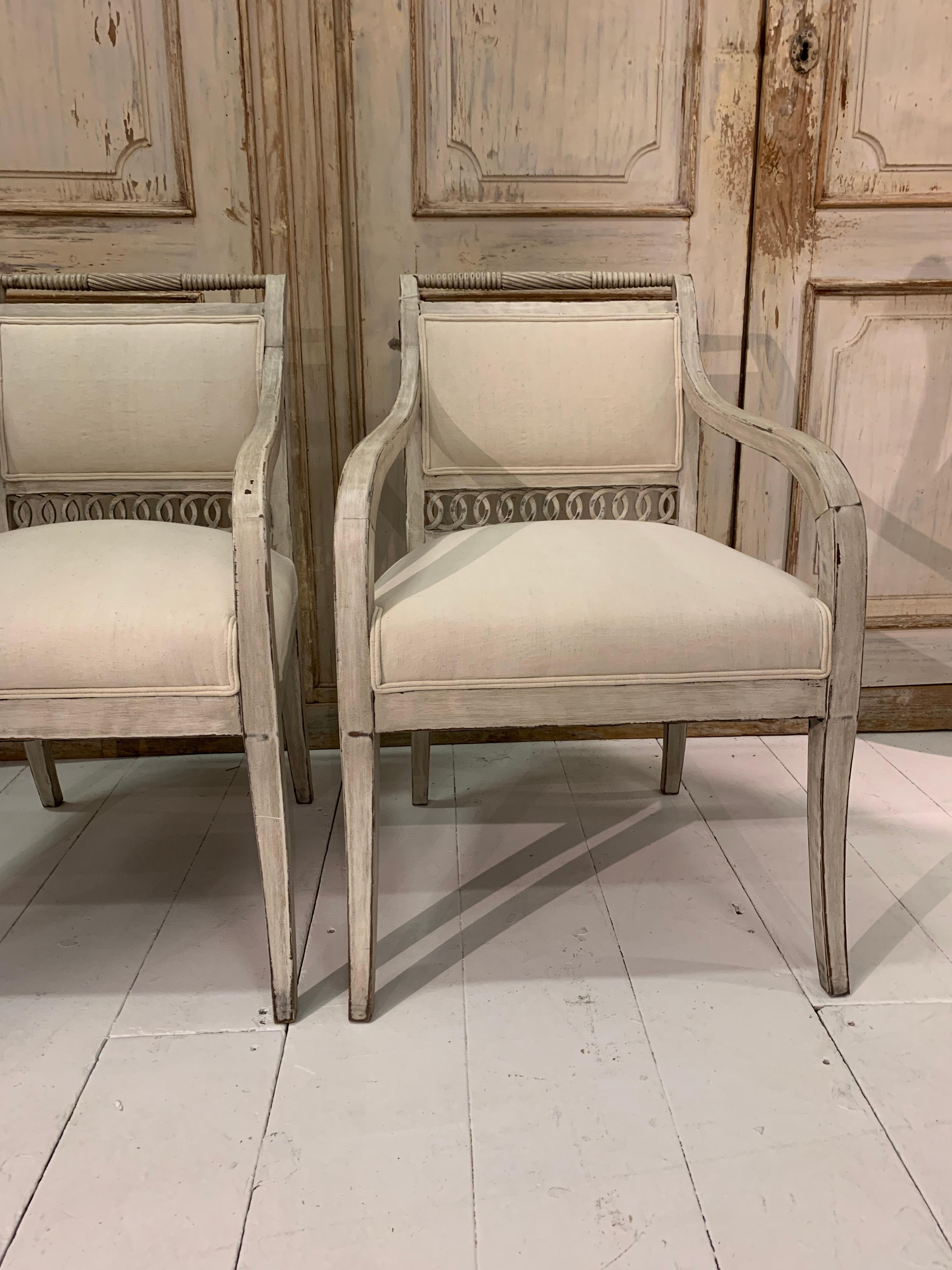A pair of charming late 19th century upholstered painted Swedish open armchairs with a decorative fretwork border detail and turned stretchers to their backs.
Recently reupholstered in a light vintage French linen.

Perfect for a bedroom or as