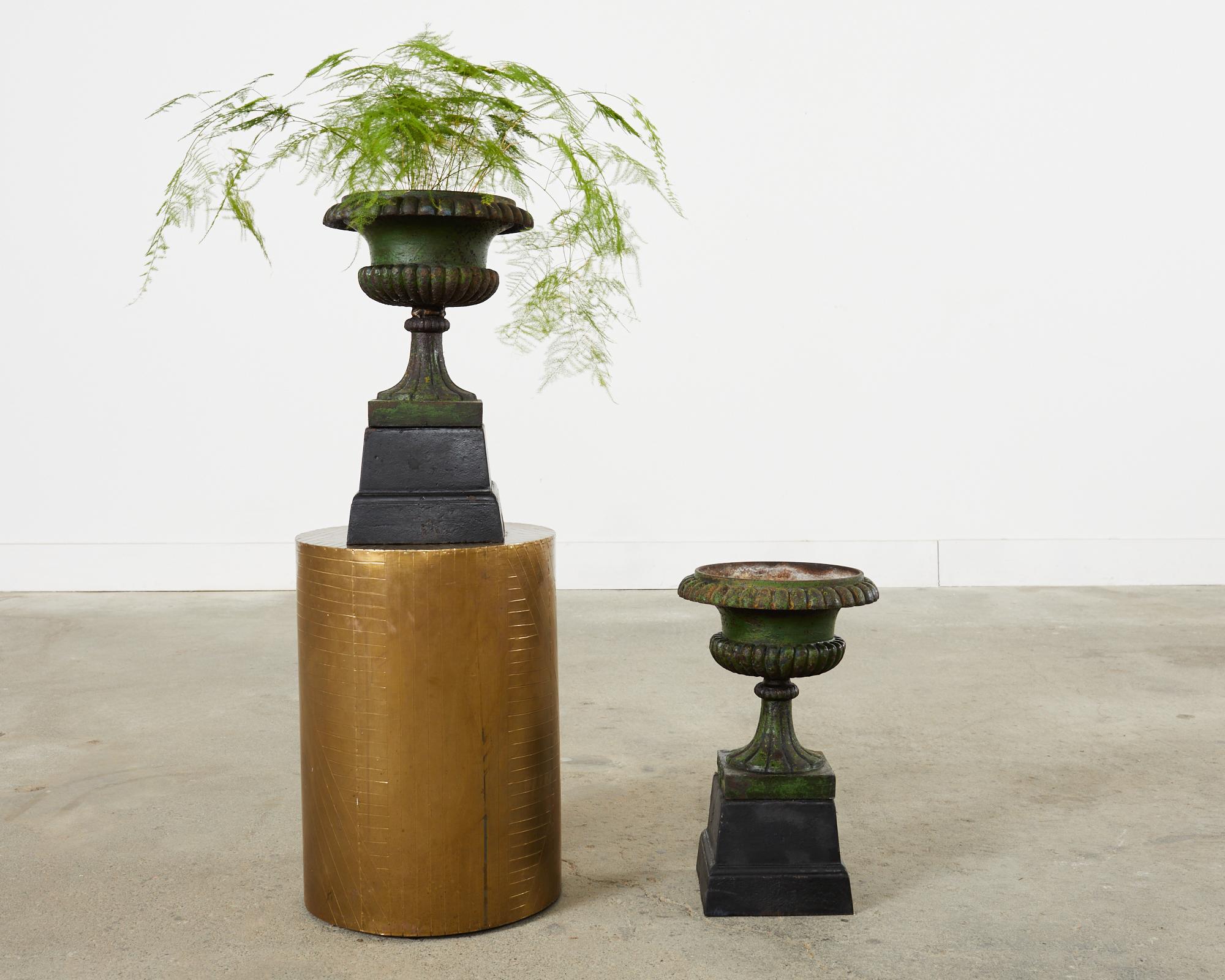 Rare pair of signed and stamped campana form urns, vases, or jardinaires made by the 17th century foundry Husqvarna in Sweden. Each urn has neoclassical style with fluted or reeded design. The vases are mounted on footed plinths or stands. The iron