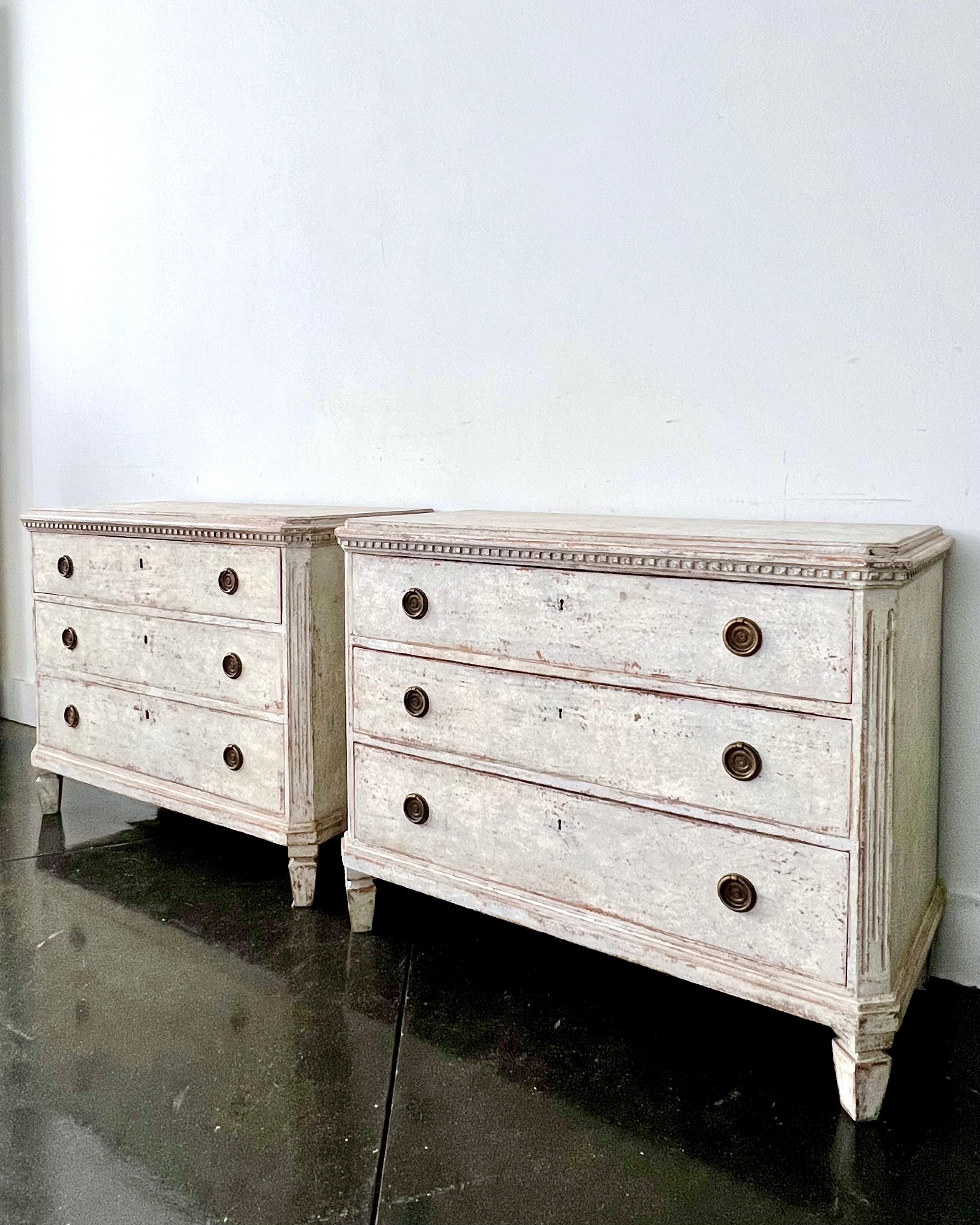 A pair of mid 19th century Swedish Gustavian style chest of drawers with brass fittings, dental trims under the shaped wooden tops, canted and fluted corners posts in light white/ grayish finish, resting on short, square tapering feet.
Sweden, circa