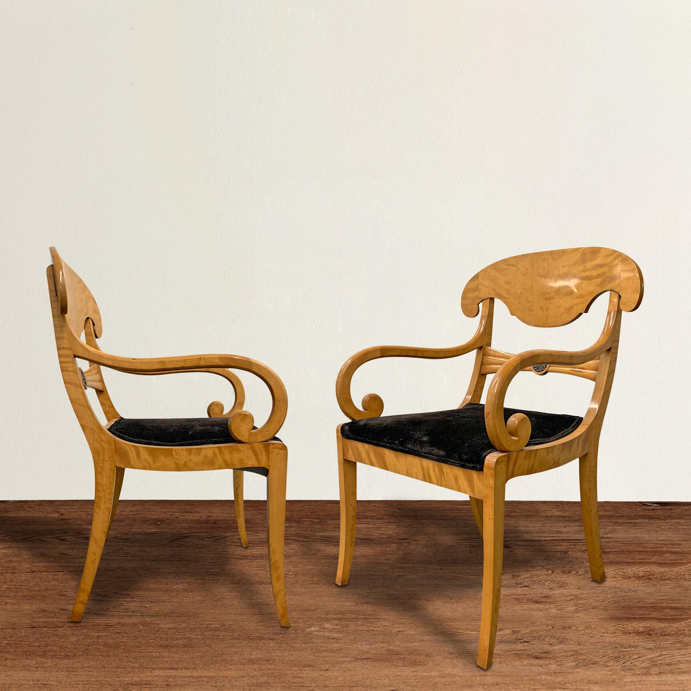 A pair of chic early 19th century Swedish Karl Johan figural birchwood chairs with elegant scrolled arms, ribbon-carved backsplats with ebonized wood carved flower rosettes, saber legs, and black velvet upholstery. The Karl Johan movement ran