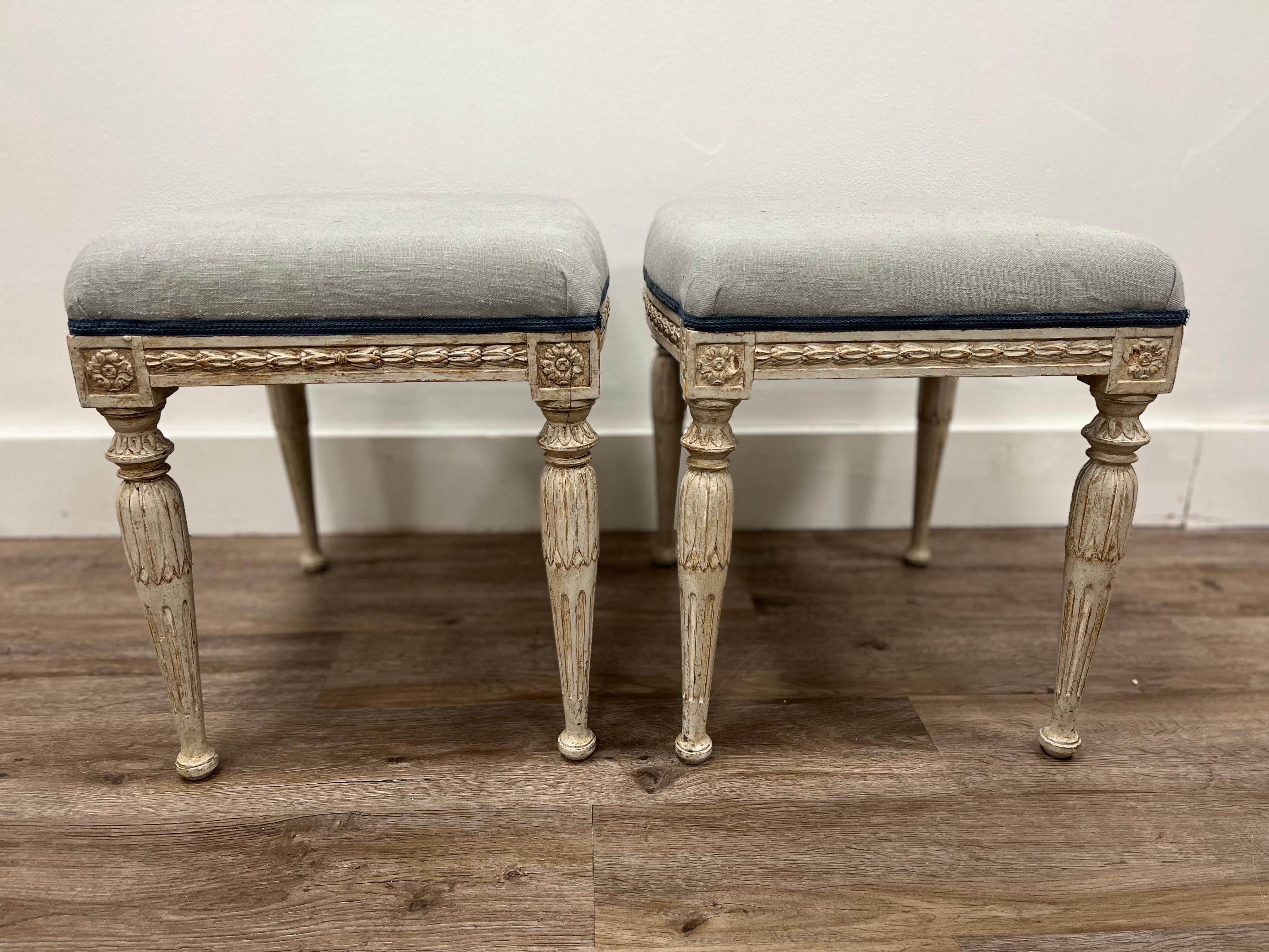 A beautiful pair of Late Gustavian footstools. In the style of Ephraim Ståhl. Rectangular frame with slight bowfront and back. Featuring a decorative hand-carved scroll with fleurons on the corners. Turned legs have leaf cut over-collaring and