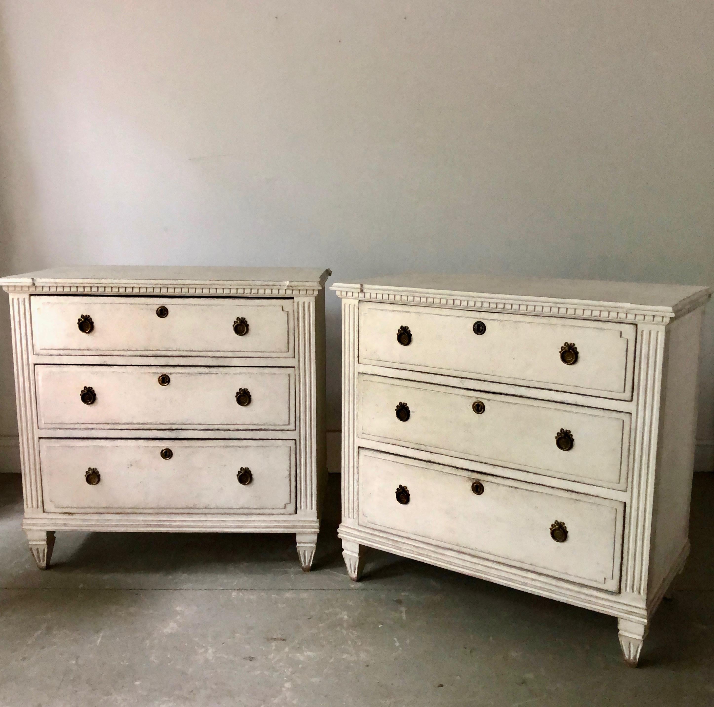 19th century Swedish Gustavian style chests in old white paint with marbleized wooden tops. Drawers with raised panels and bronze hardwares. Canted corner post with dentil molding under the shaped top on tapering reeded and fluted legs. 

Here are