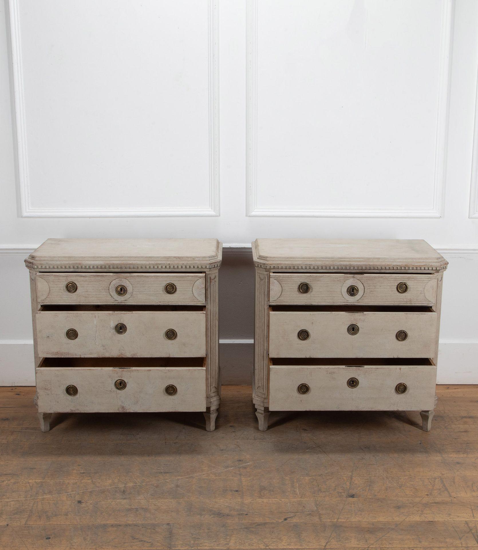 A pair of Swedish 19th Century painted Gustavian style commodes.
With three drawers, reeded decoration and canted corners square tapered legs.
Painted in an off white grey paint with brass hardware.
Circa 1890.