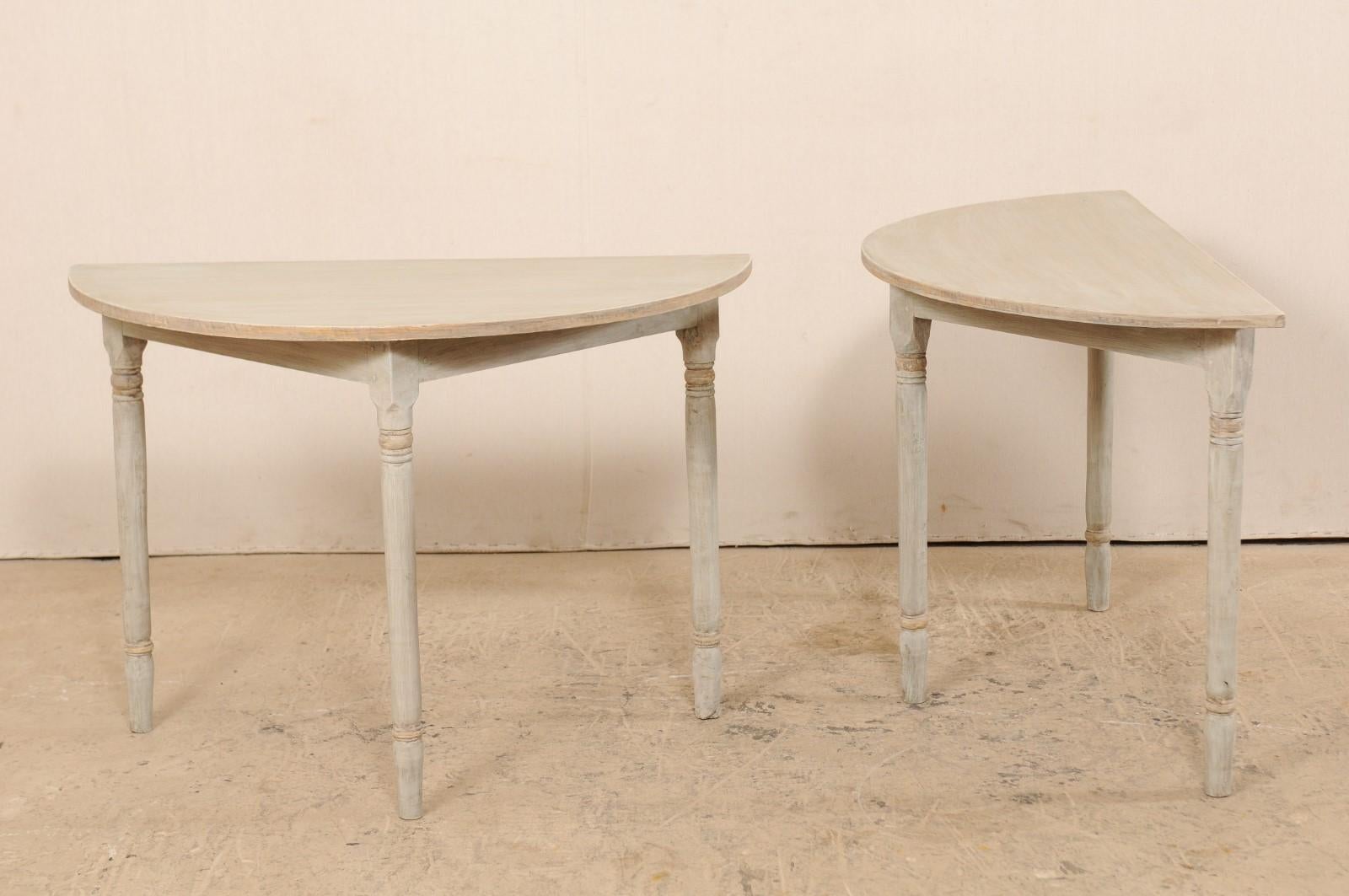 A pair of 19th century Swedish painted wood demilune tables. This pair of antique demilune tables from Sweden each features half moon tops over triangular-shaped aprons, and are raised on three rounded legs with turned carvings accentuating their