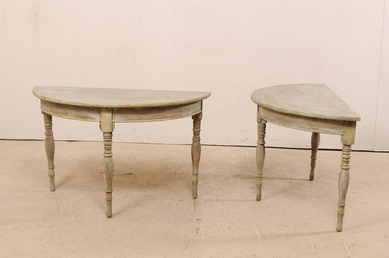 A pair of 19th century Swedish demilune tables. This pair of antique Swedish painted wood demilune tables features half moon tops over rounded aprons. The pair is raised on three beautifully turned legs. These demilune consoles tables have a