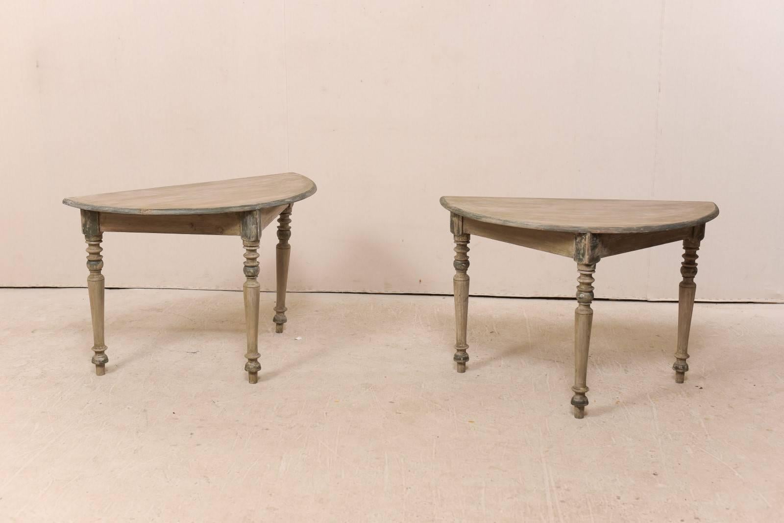 A pair of 19th century Swedish painted wood demilune tables. This pair of antique painted wood demilune tables from Sweden feature half moon, semi-circular tops over triangular aprons. The tables are presented upon three beautifully turned legs.