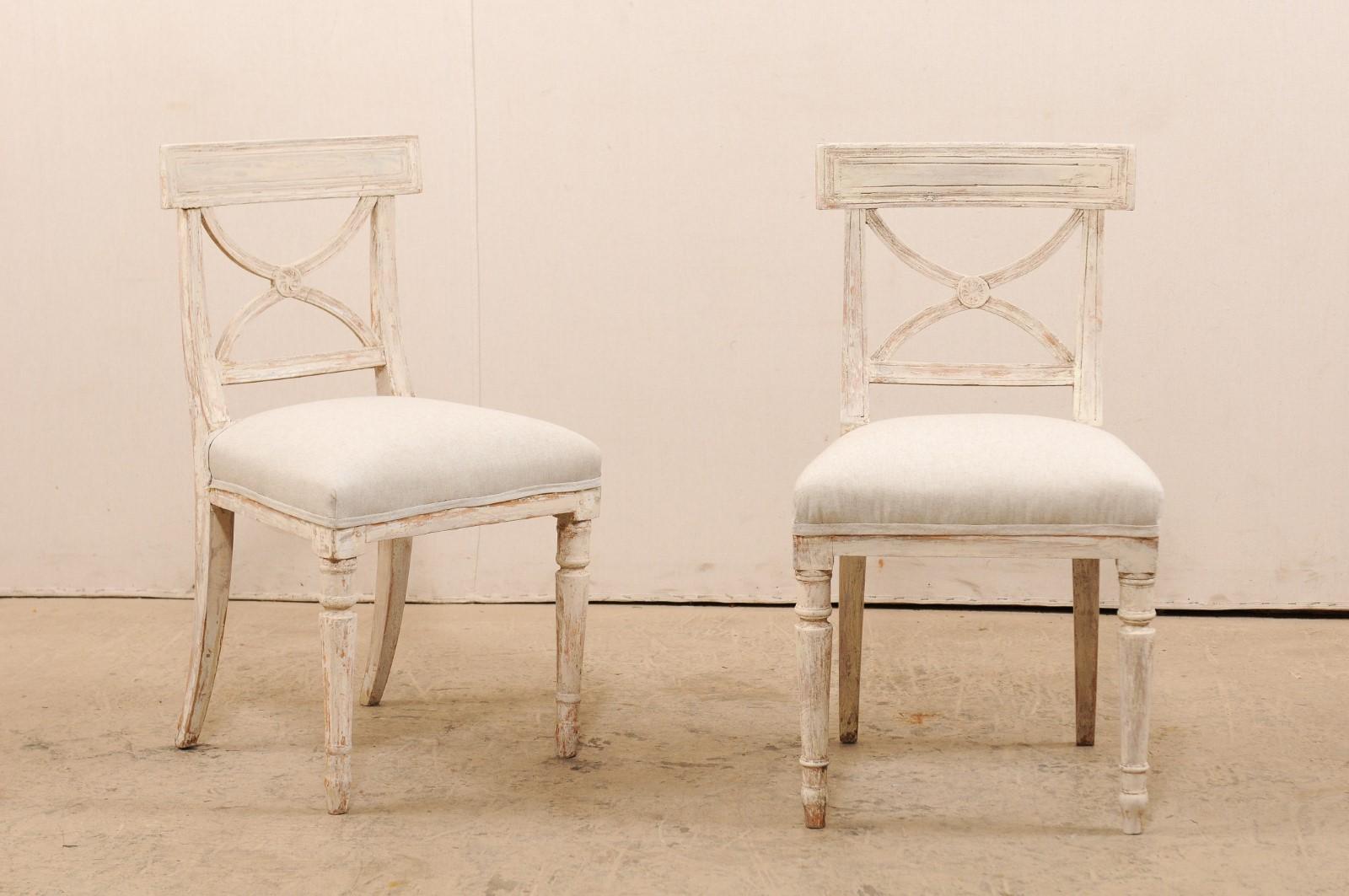 A pair of Swedish period Gustavian side chairs from the 19th century. These antique chairs from Sweden have an airy design quality to them with their open style backs, topped with a rectangular-shaped upper top rail which frames the elegant cutout
