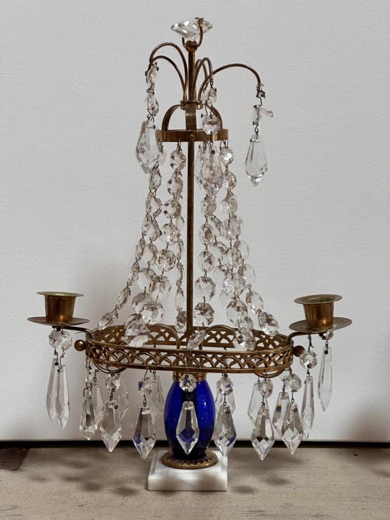 Pair of 19th Century Swedish two-light girandoles or candelabra, having draping crystals,  the candle holders supported by an oval brass ring over a cobalt blue glass vase-form support  on marble plinths.
