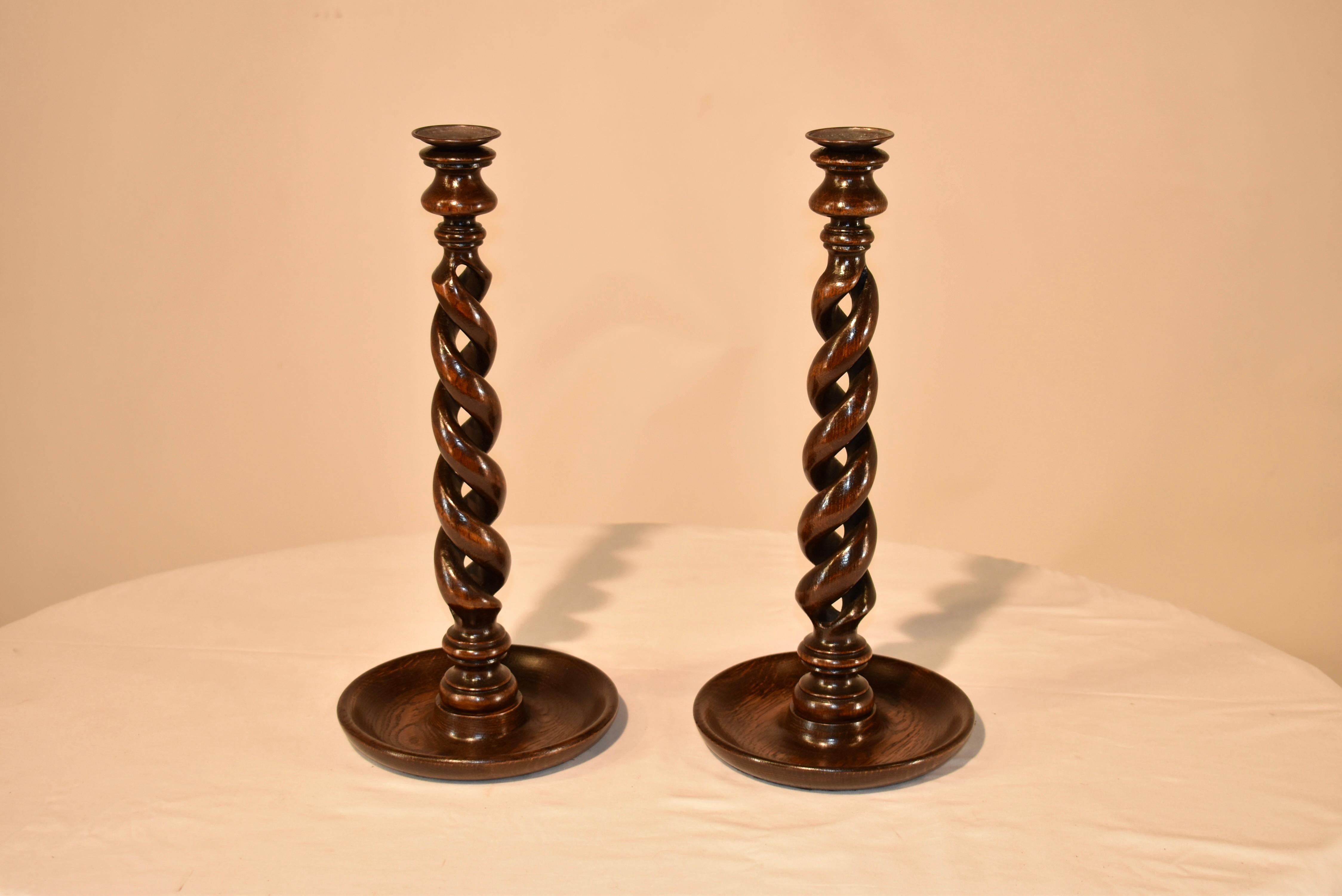 Pair of 19th century English oak tall candlesticks. They have brass bobeches over hand turned candle cups, supported on exquisitely hand turned open barley twist stems. The bases are hand turned dish shaped bases and the overall height is 16.25