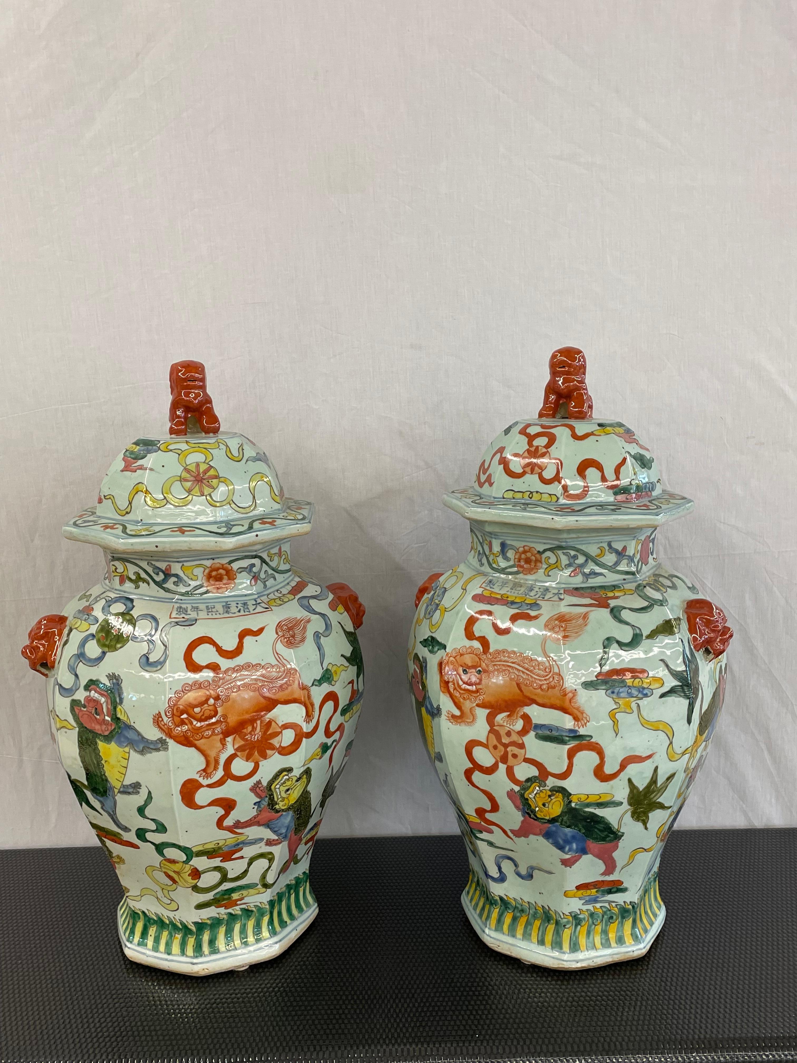 Pair of 19th Century Temple Jars. Each having a wonderful color scene depicting vibrant dragons, flowers and geometric designs. Each signed on the front. The pair having Foo Dog Lids. This large and impressive pair measure 27 inches with the lids