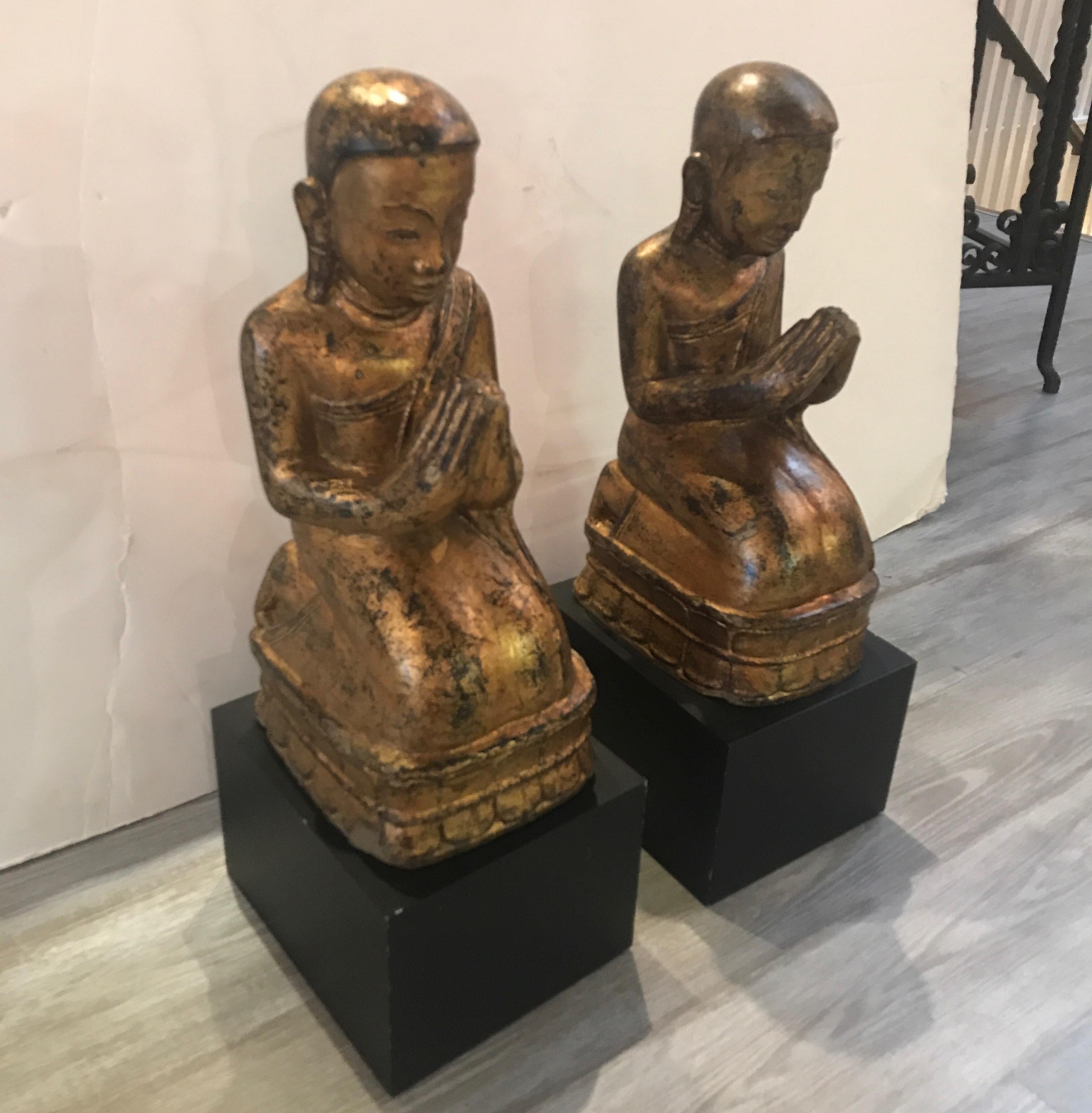 19th century pair of gilt decorated Thai terracotta temple monks on later custom bases. An original pair with a weathered gold surface resting on a flat black cube base.