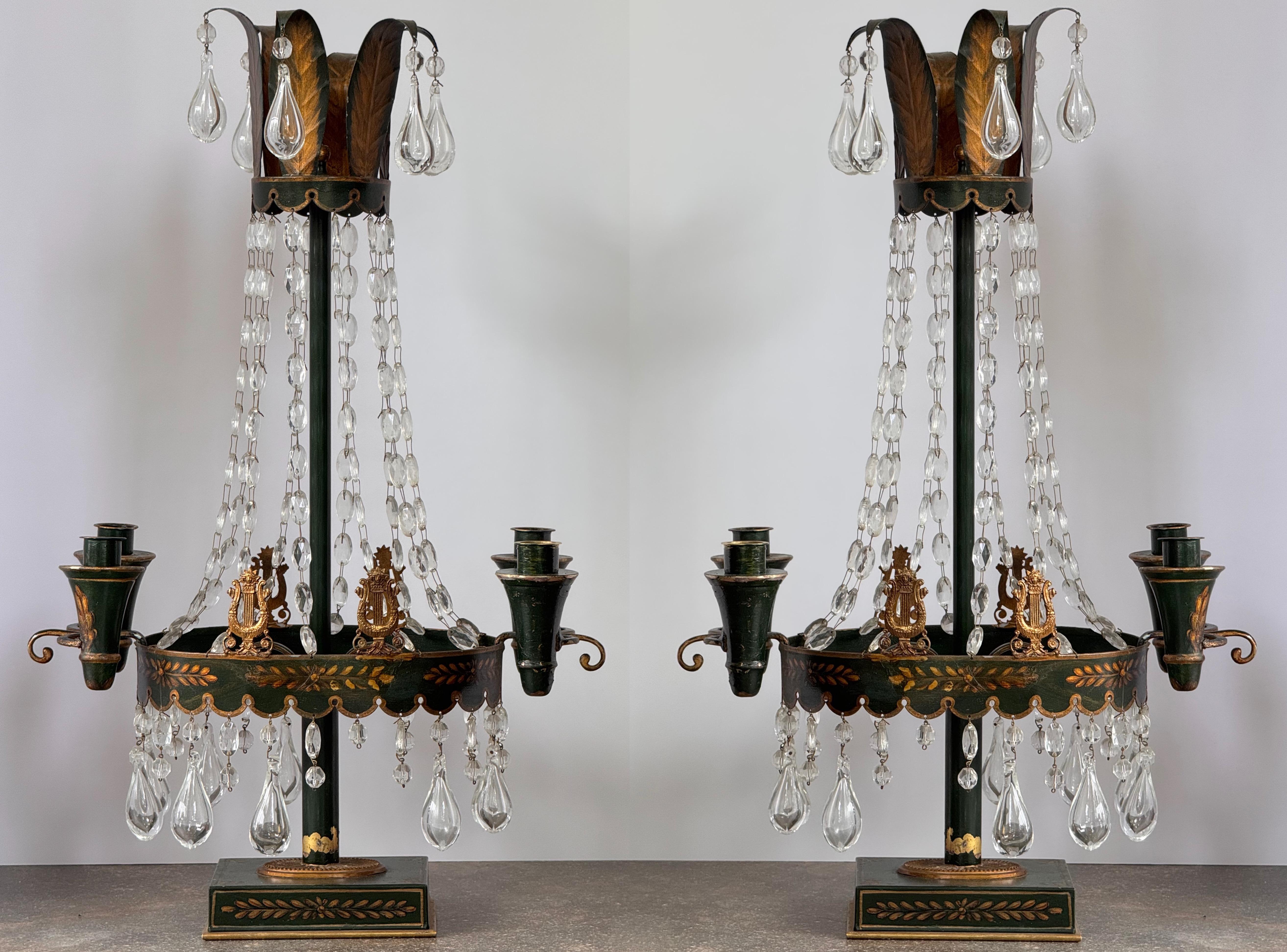 Elegant pair of 19th century tôle candelabra painted deep green with gilt foliate decoration. Each piece features two candle arms, draped with faceted crystal chains and large teardrop prisms. The round gallery is adorned with applied gilt lyres and