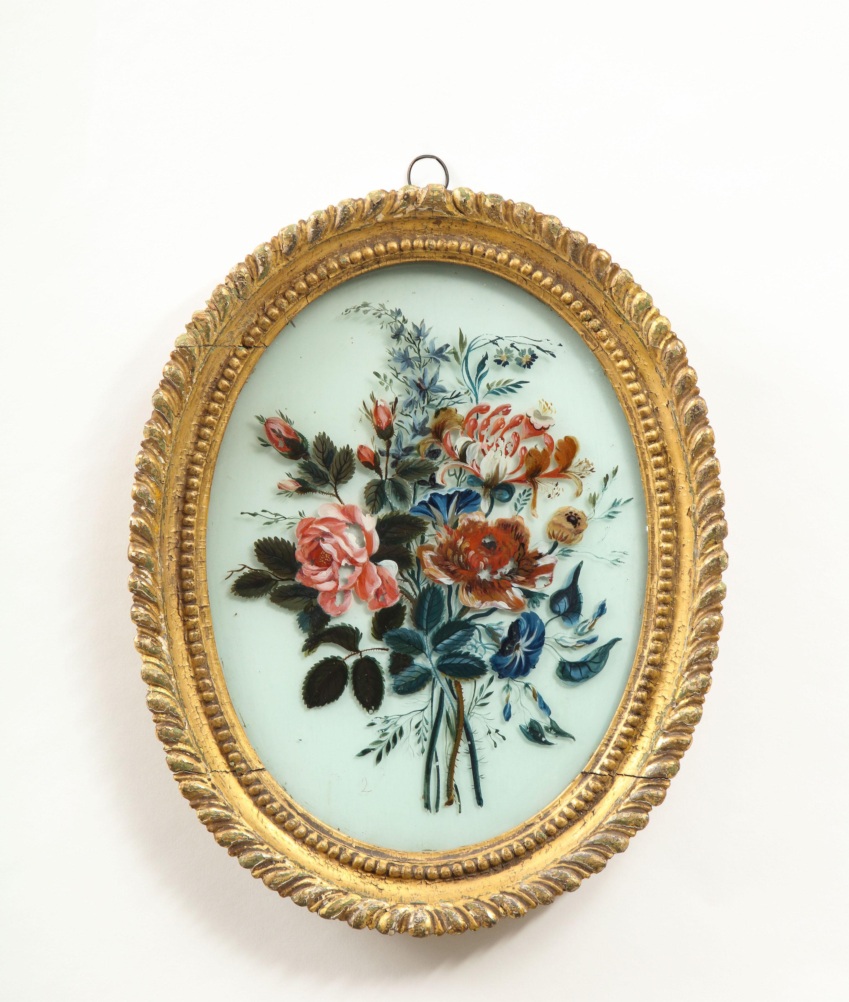 Each within an oval gilt gesso frame molded with foliate and beaded banding, depicting a floral bouquet including roses, morning glory, peonies, phlox and auricle, on a white glass ground.