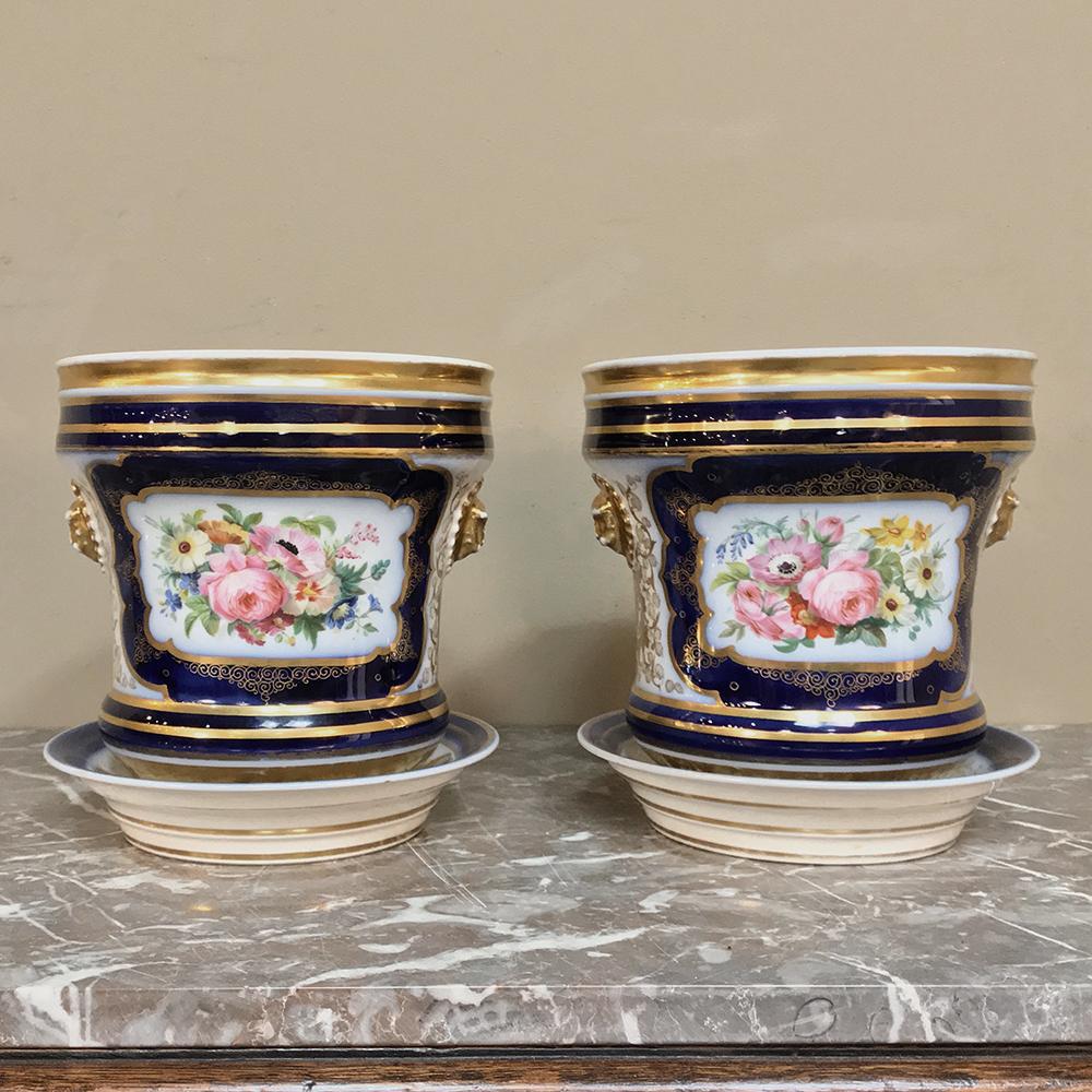 Pair of 19th century Vieux Paris porcelain hand-painted cachepots feature a traditional urn shape with coasters underneath for overflow water. An abundant use of gold trim contrasts nicely with the soft pastel floral bouquet cameo paintings set on a