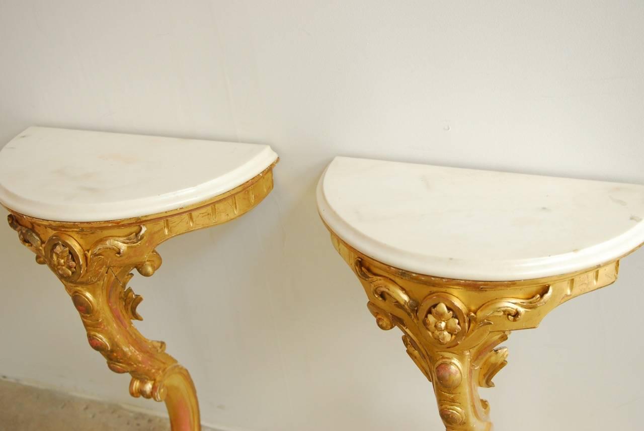 Fantastic pair of Italian 19th century wall-mounted console tables. Featuring a hand gilt carved base topped with a demilune white marble. Each piece is dramatically carved and covered in gold leaf with a serpentine leg. The white marble tops have
