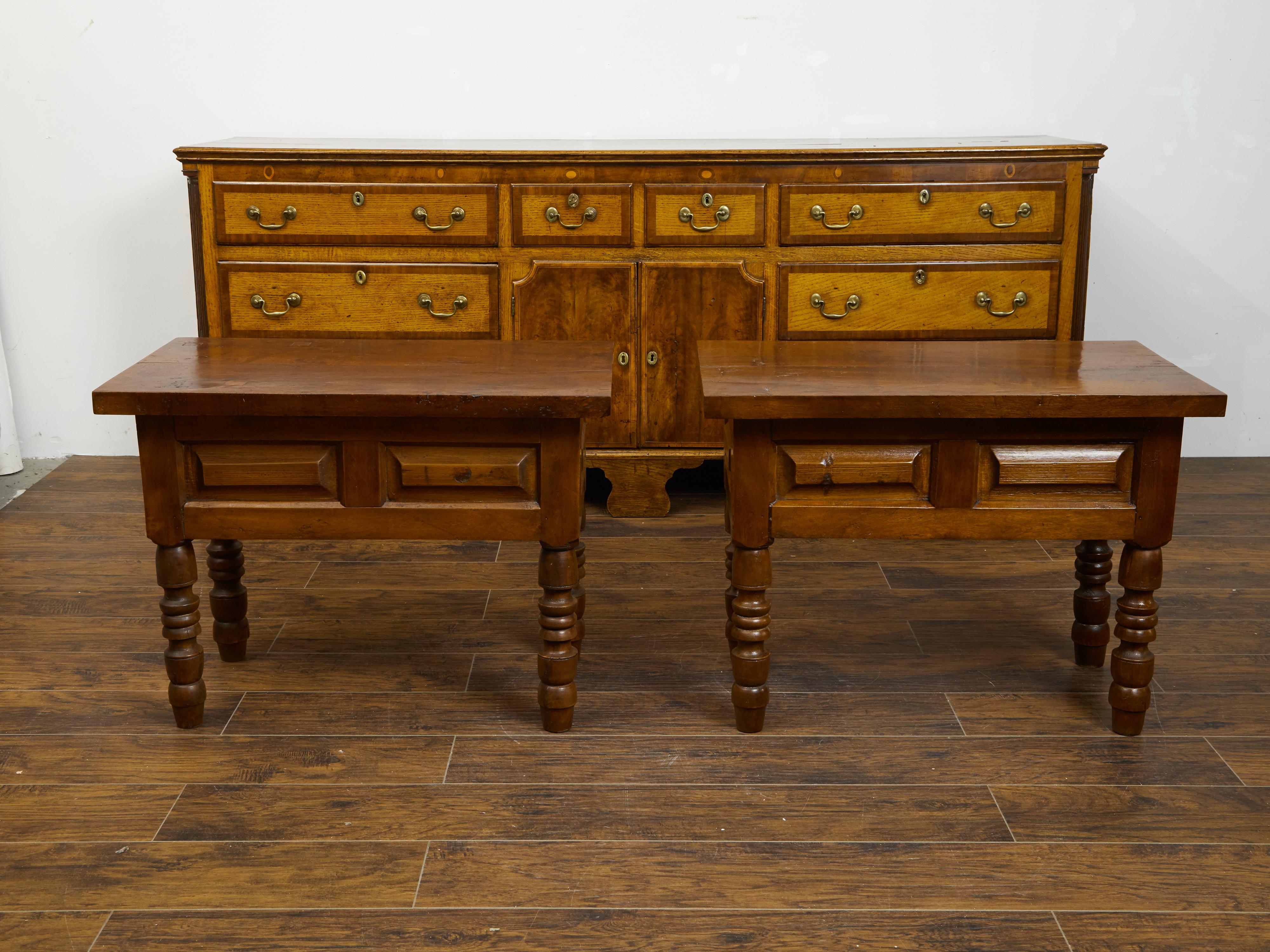A pair of Continental walnut side tables from the 19th century, with raised panels and turned legs. Created during the 19th century, each of this pair of Continental side tables features a rectangular top sitting above an apron adorned with raised