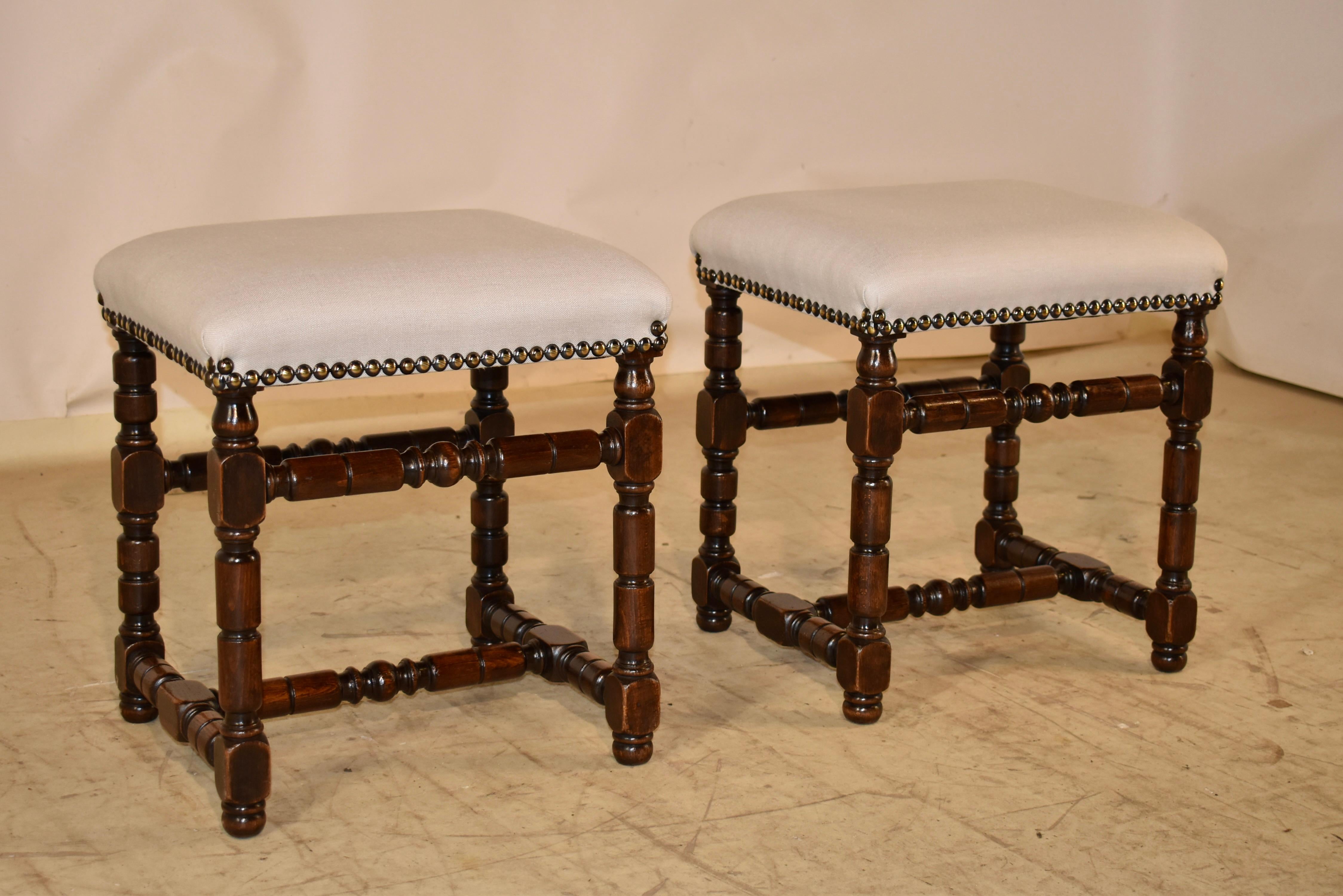 Pair of 19th century turned walnut upholstered stools from France.

The seats, newly upholstered in cotton and finished with a decorative brass nail head trim, and following down to hand turned legs, joined by matching stretchers.  The stools are