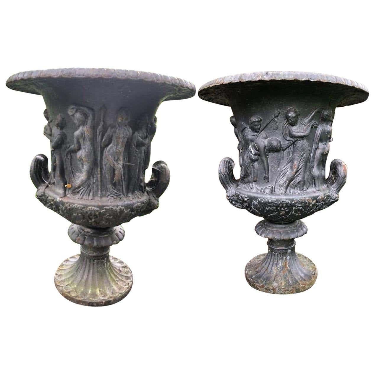 A pair of 19th century weathered cast iron urns after the Medici and Borghese models. Classic egg and dart overhanging rim, above a waisted body cast in relief with a continuous scene of mythological figures, the acanthus lower section flanked to