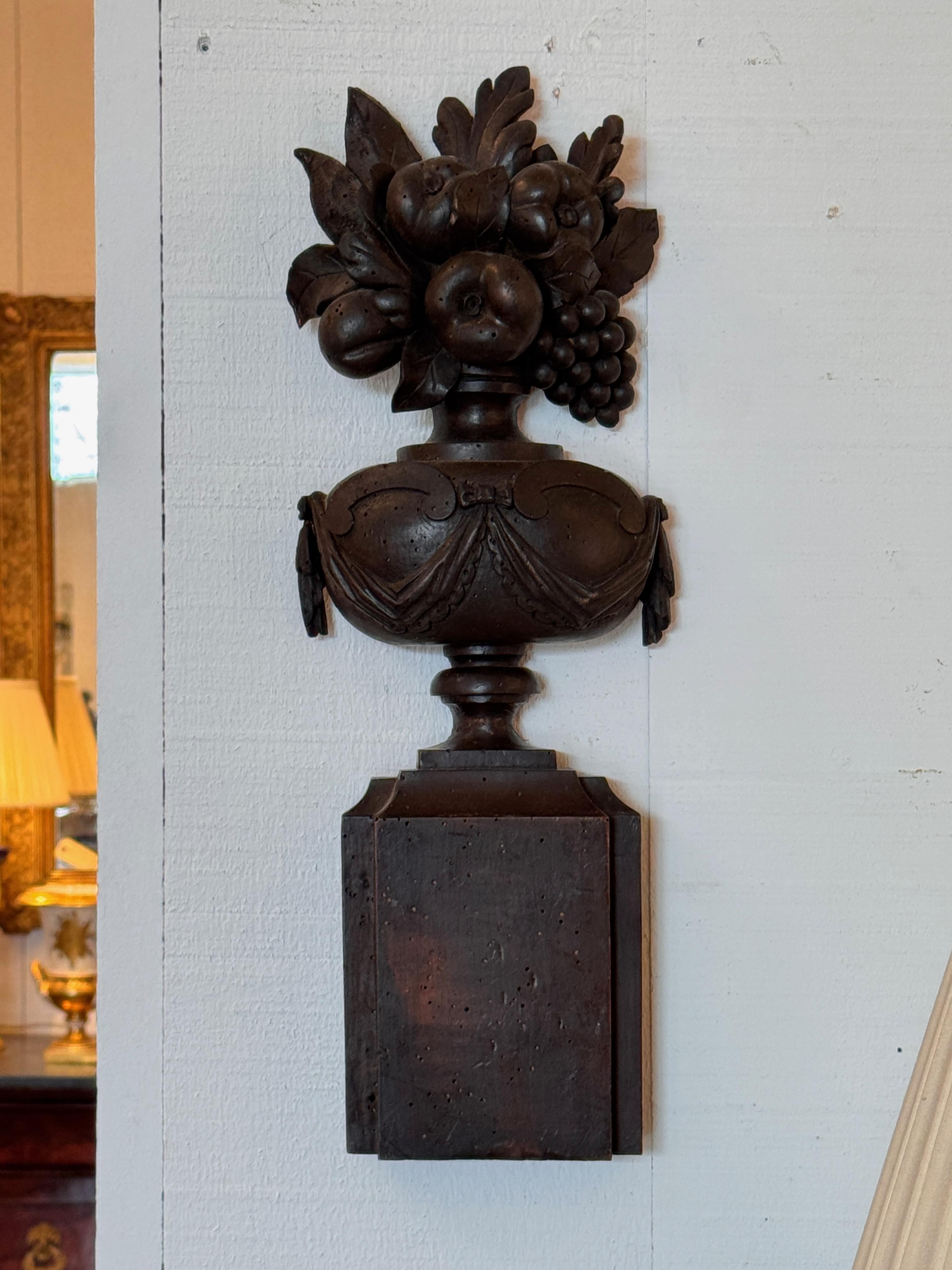 Deeply carved wood urns in relief, each topped with an abundant arrangement of fruit and foliage. Swag details on the urn bodies and a dark, aged finish add classic decorative appeal. Sold as a pair.