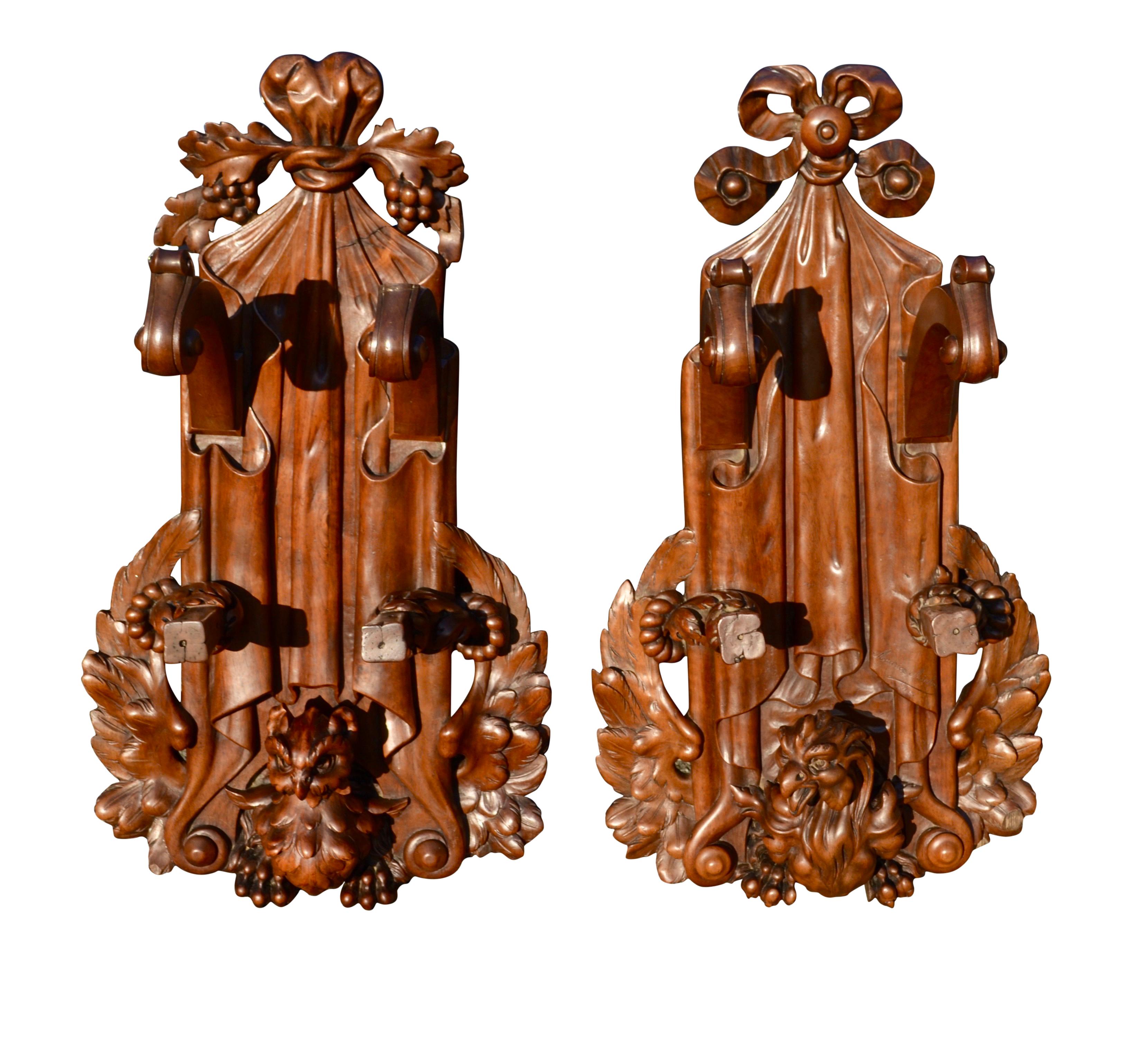 A highly rare and most unusual pair of carved walnut gun racks, each with a different carved bird at the bottom, one being a hawk or eagle with spread wings and talons along the bottom; the second bird looking more like an angry owl, also with