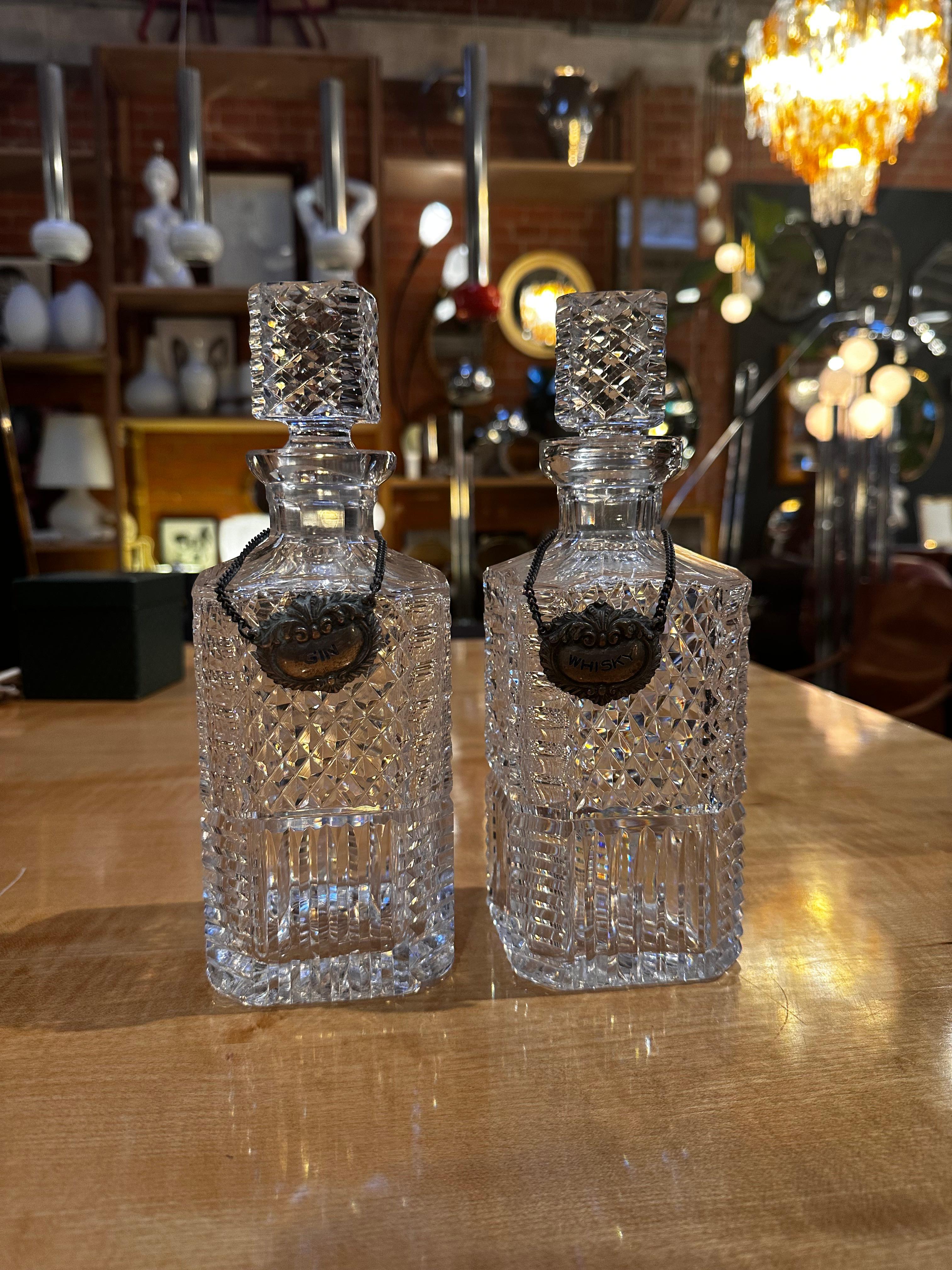 A Pair of 2 Crystal Decanters from the 1960s, one designed for gin and the other for whiskey, are exquisite examples of mid-century barware. Crafted from high-quality crystal, these decanters showcase the elegance and attention to detail