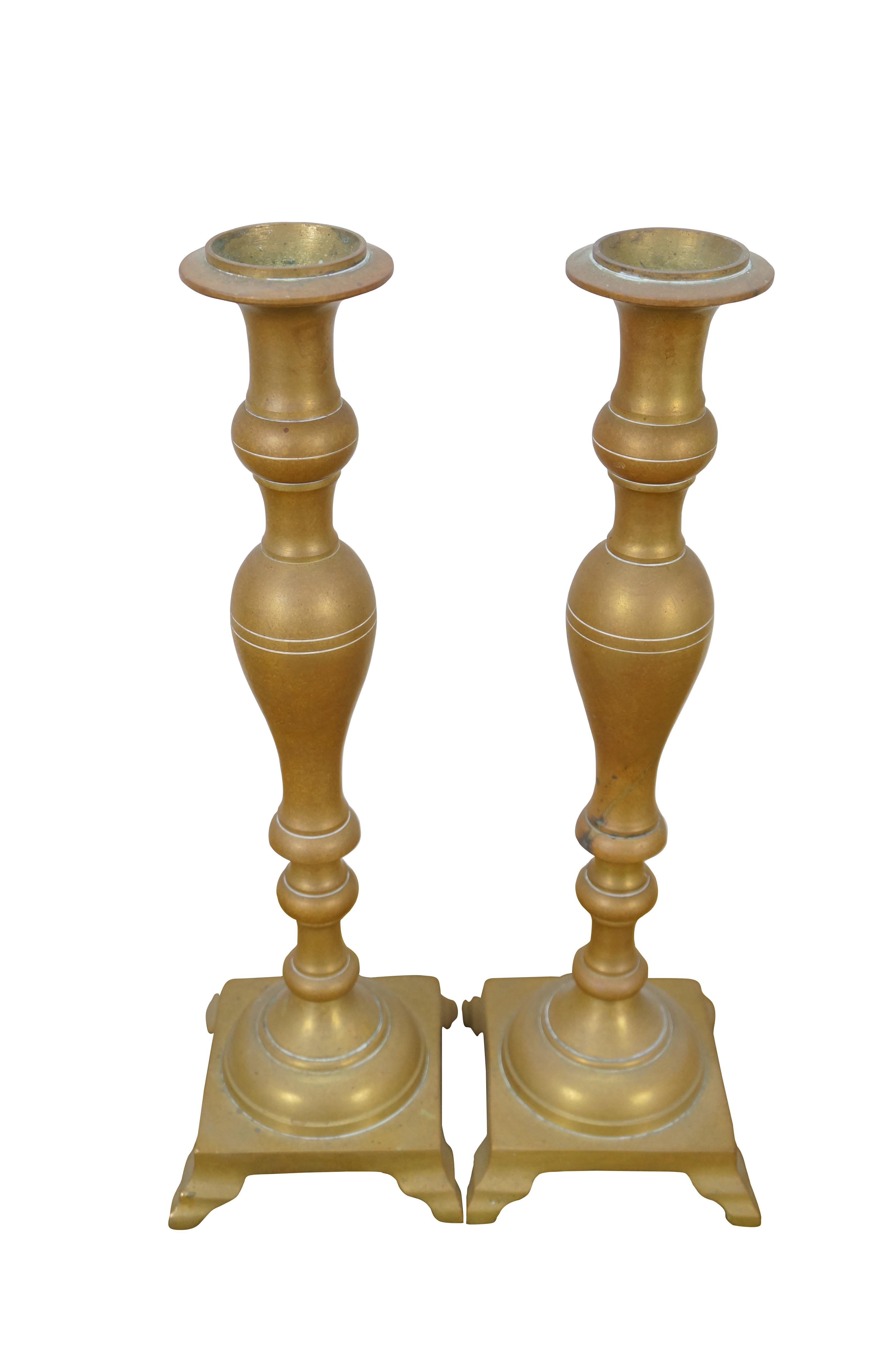 Coppia di candelabri alti, vintage, in ottone massiccio. Basi quadrate con piedi inclinati e design a balaustro tornito. 

Dimensioni:
5,75