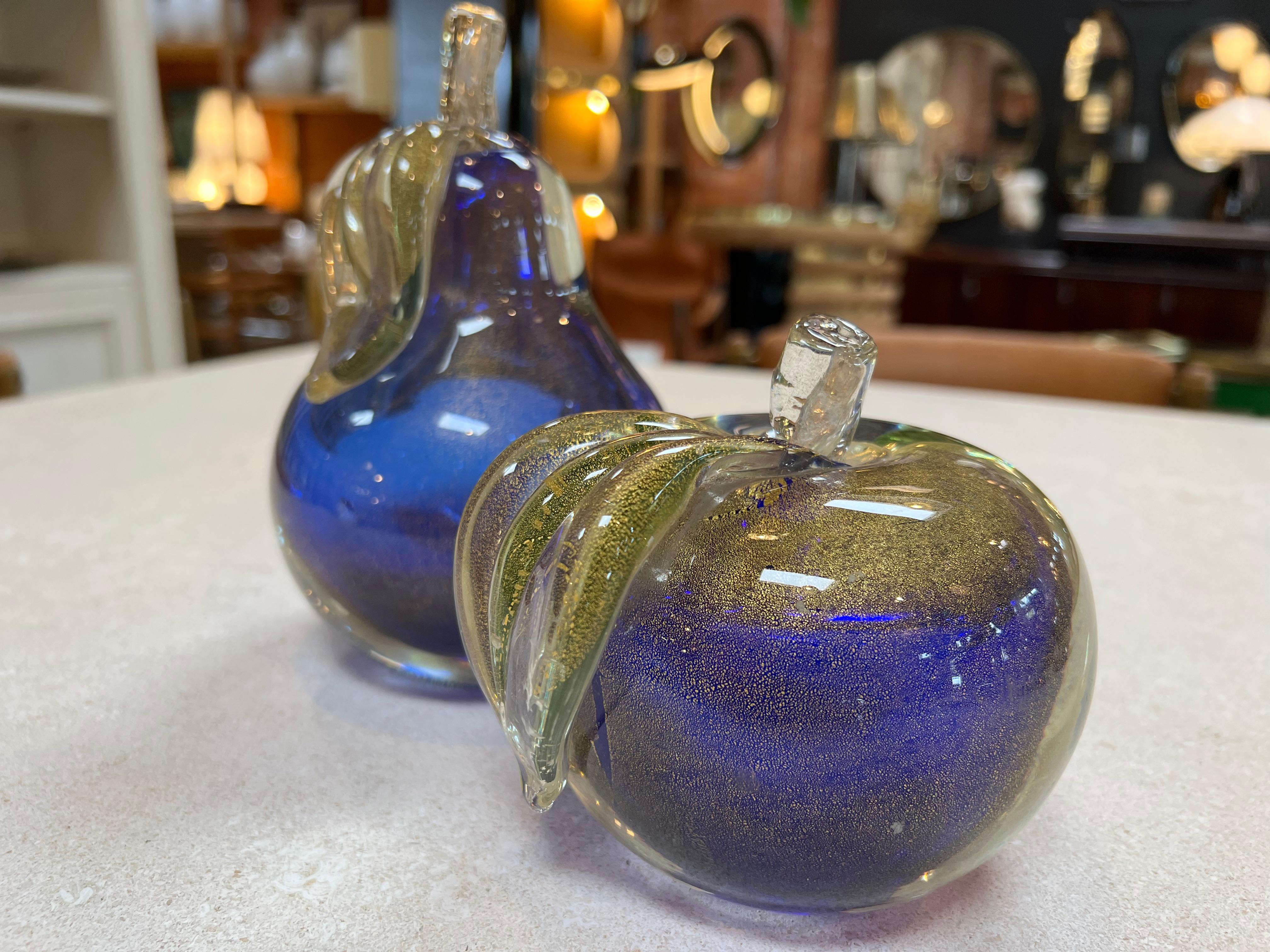 Behold the captivating duo of exquisite decorative objects crafted from the finest blue Murano glass. This enchanting set features two charming apple figurines and one elegant pear sculpture, each meticulously hand-blown to perfection. The radiant