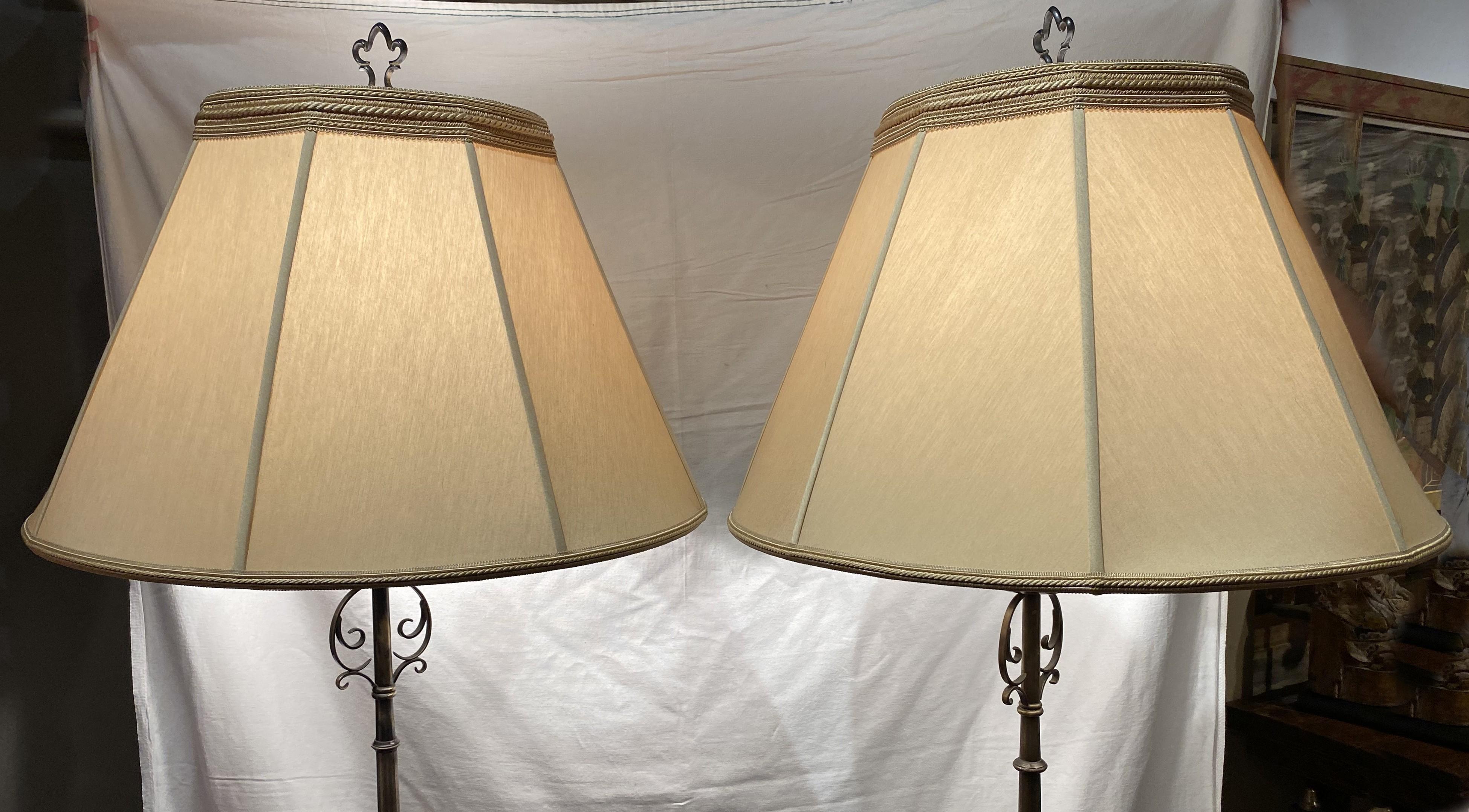 Une belle paire d'objets en métal forgé à la main  Lampadaires torchères, chacun avec une seule lumière, manchon de bougie, poteau tourné, abat-jour de qualité design, épis de faîtage en fleur de lys,  et des bases tripodes à volutes. Les lampes