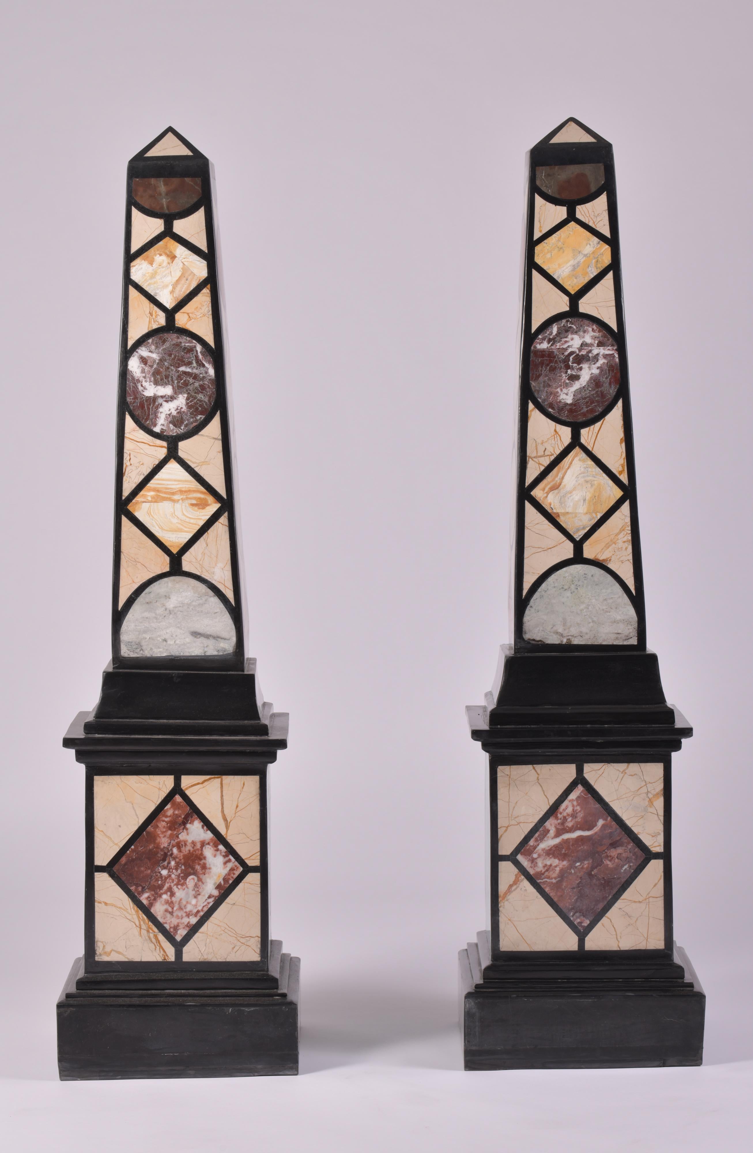 This sleek and very decorative pair of marble specimen obelisks set on a cubed base features a geometric designed pattern in green, purple, cream and brick red all outlined in black. Each obelisk measures 12 in – 30.5 cm square and 47 ½ in - 120.6