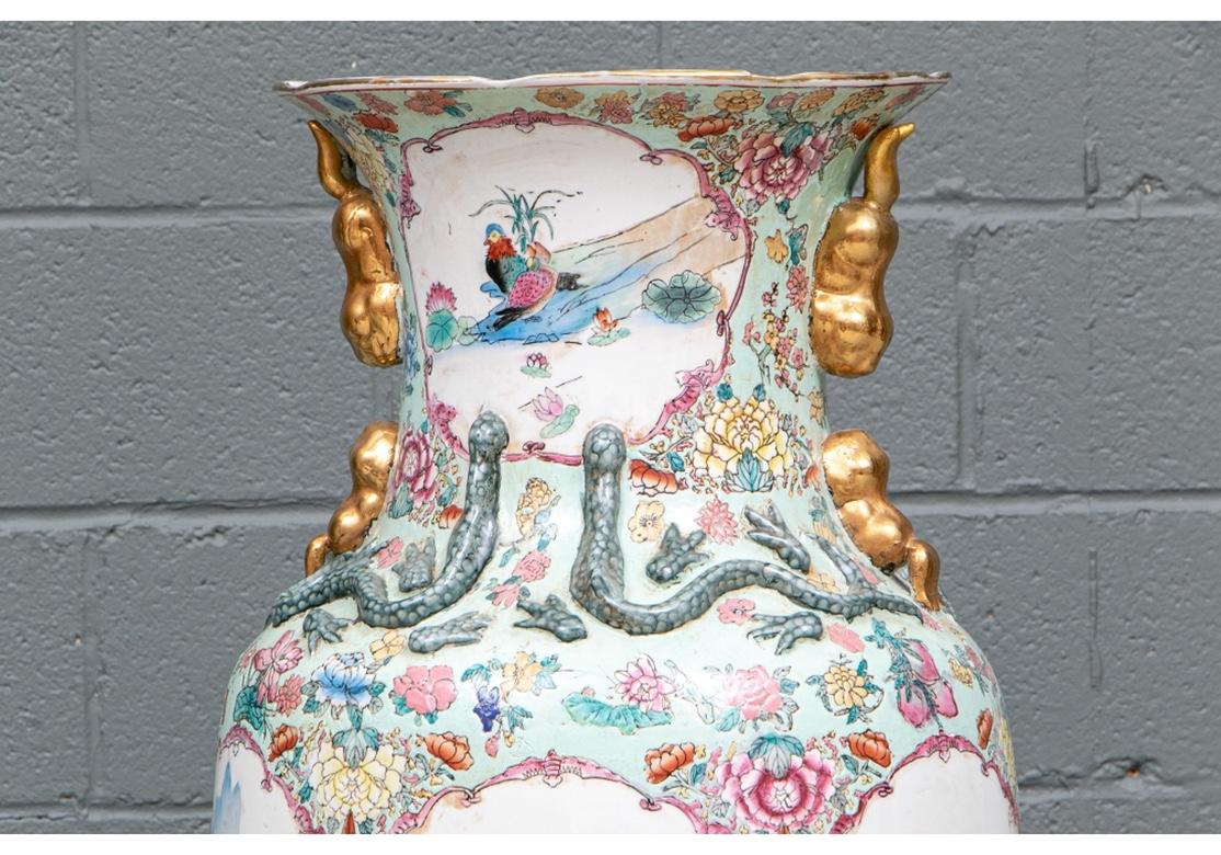 The vases decorated with birds near a lily pond and perched in flowering trees. The green glazed shoulders with multicolored flowers and green reptiles in relief. Each side with gilt stylized foo lions. Irregularly white glazed inside necks and base
