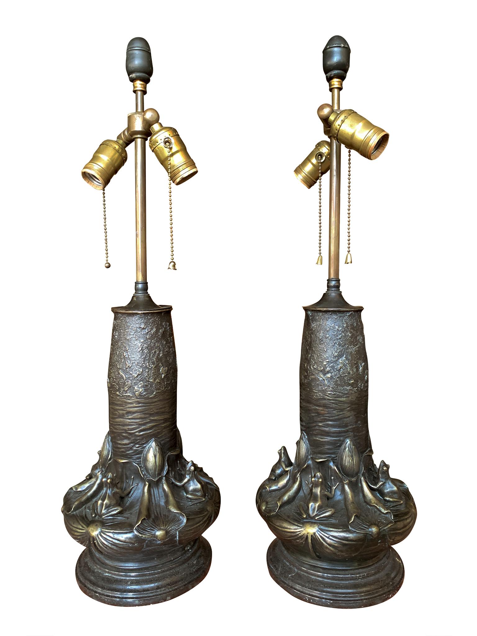 A pair of 20th century bronze table lamps in the Art Nouveau style by Jean Bunand. The body is decorated with frogs sitting poised on lily pads and gazing at the flying insects above them. The round bases are black marble. Each lamp is paired with