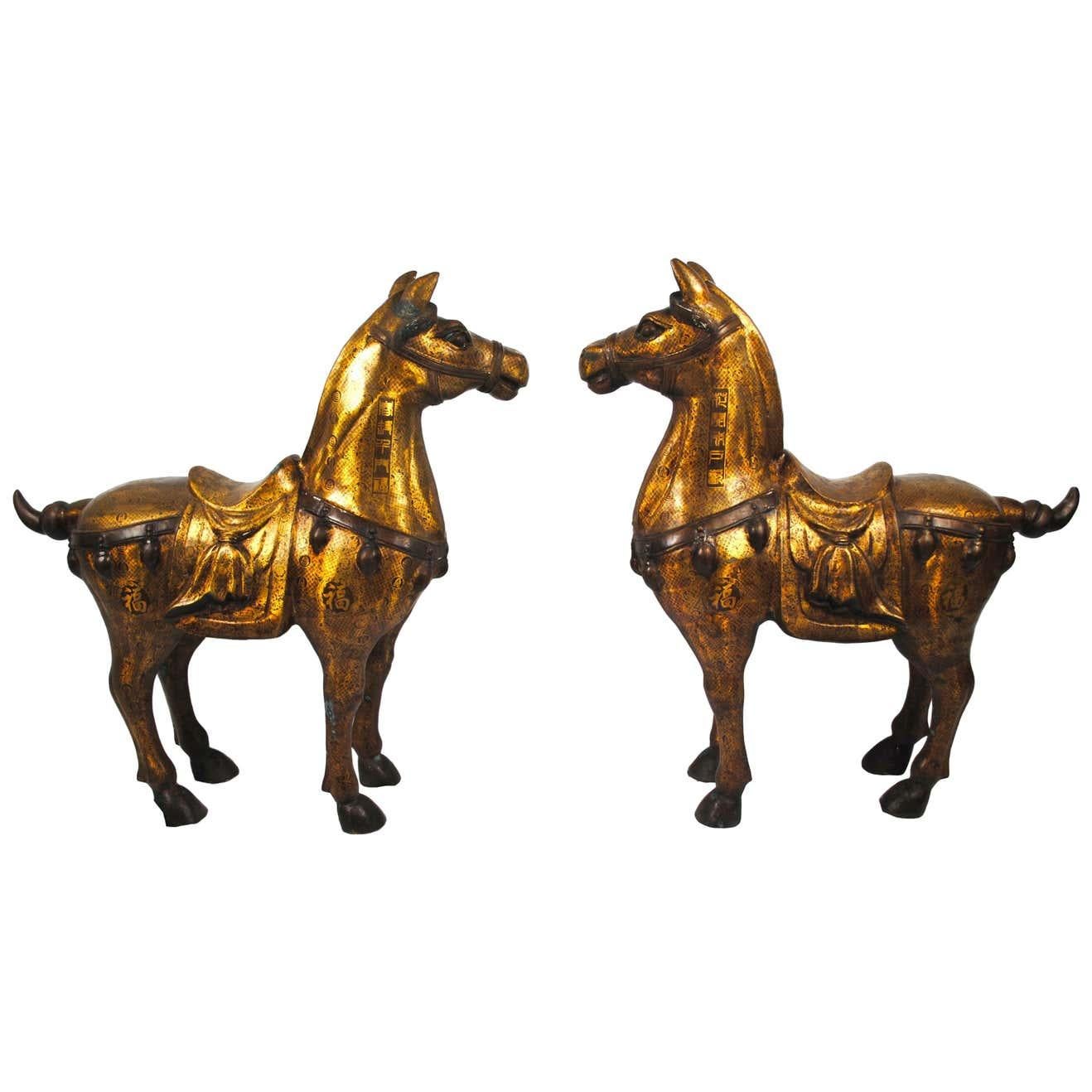 A pair of 20th century bronze gilded gift horses. Lavish pair of cast brass and gold gilt horse statues or sculptures made in the Chinese Tang dynasty style. Features intricately cast bodies with detailed Chinese characters echoed over the both