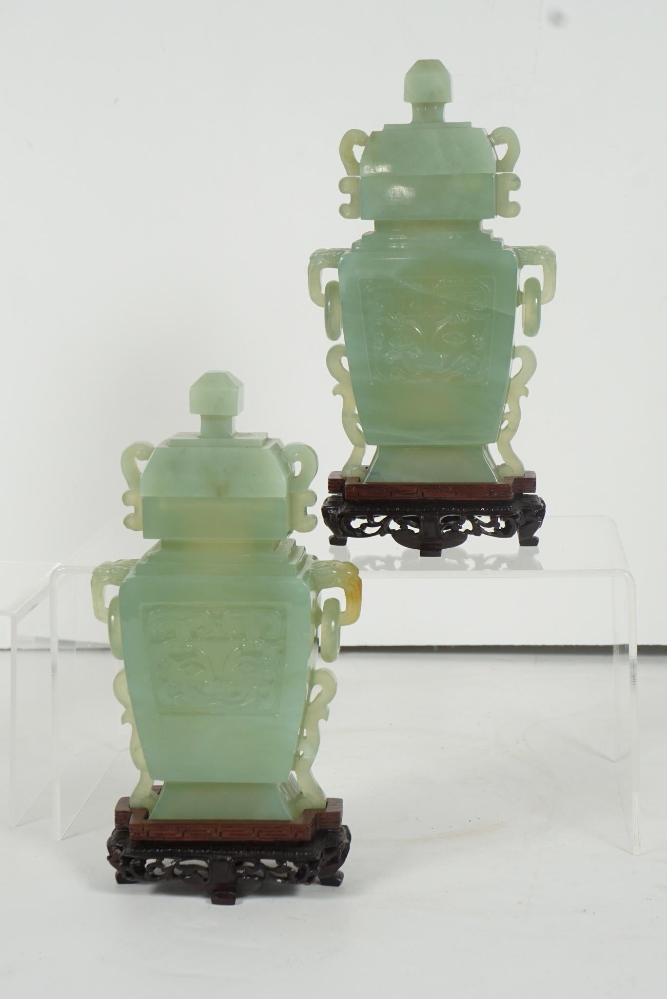 Cette belle paire d'urnes à couvercle sculpté est fabriquée en Bowenite, une pierre semi-précieuse dont on pense qu'elle ressemble au jade. Elles ont été sculptées au milieu du XXe siècle et sont accompagnées de supports en bois de rose d'une grande