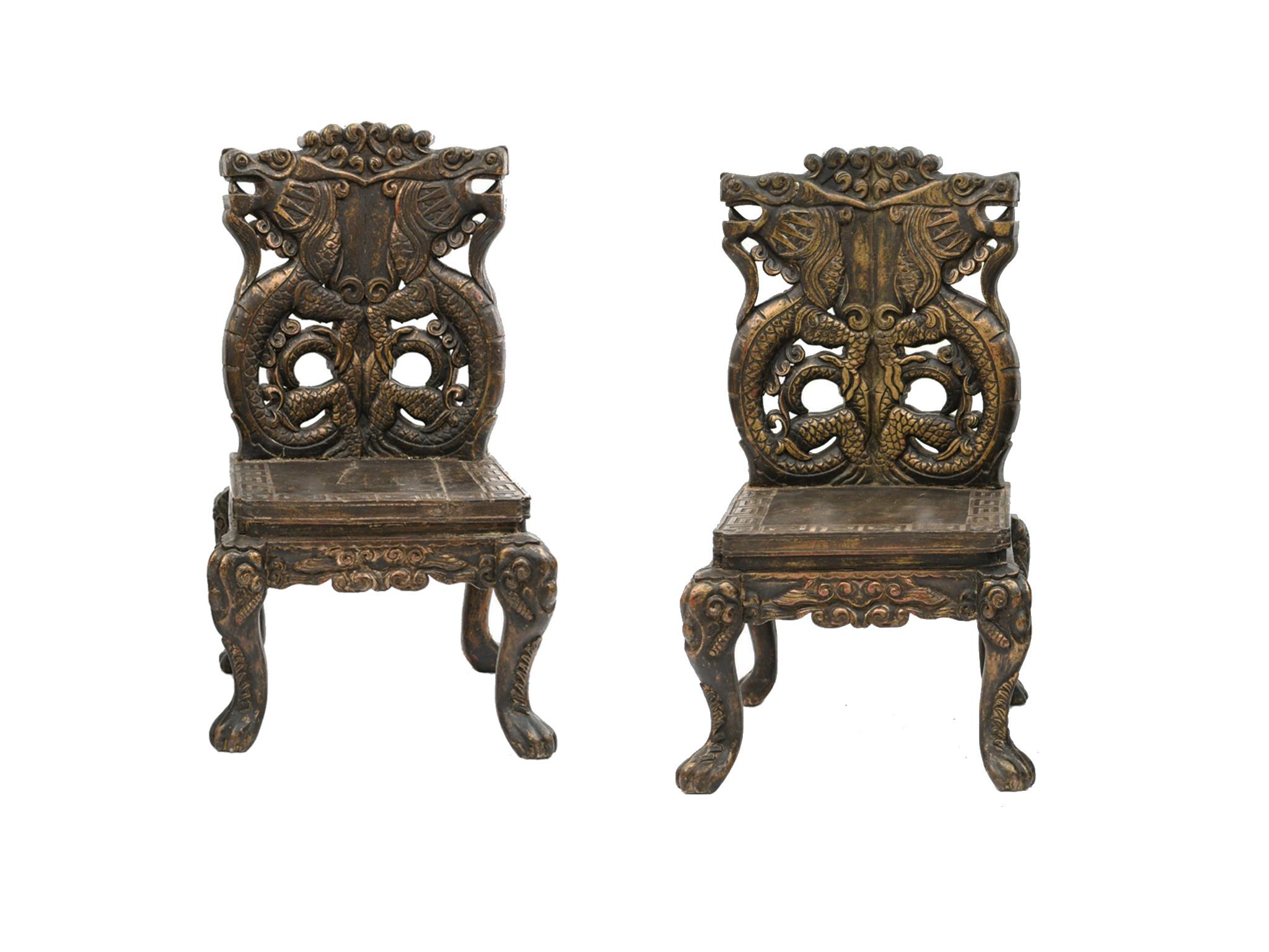 A pair of Chinese wooden chairs handmade in the 20th century. Elaborately carved twin dragons adorn the backrest, while the legs are a cabriole style that culminate in paws. The seat surface is carved with a key pattern. The chairs are antiqued with