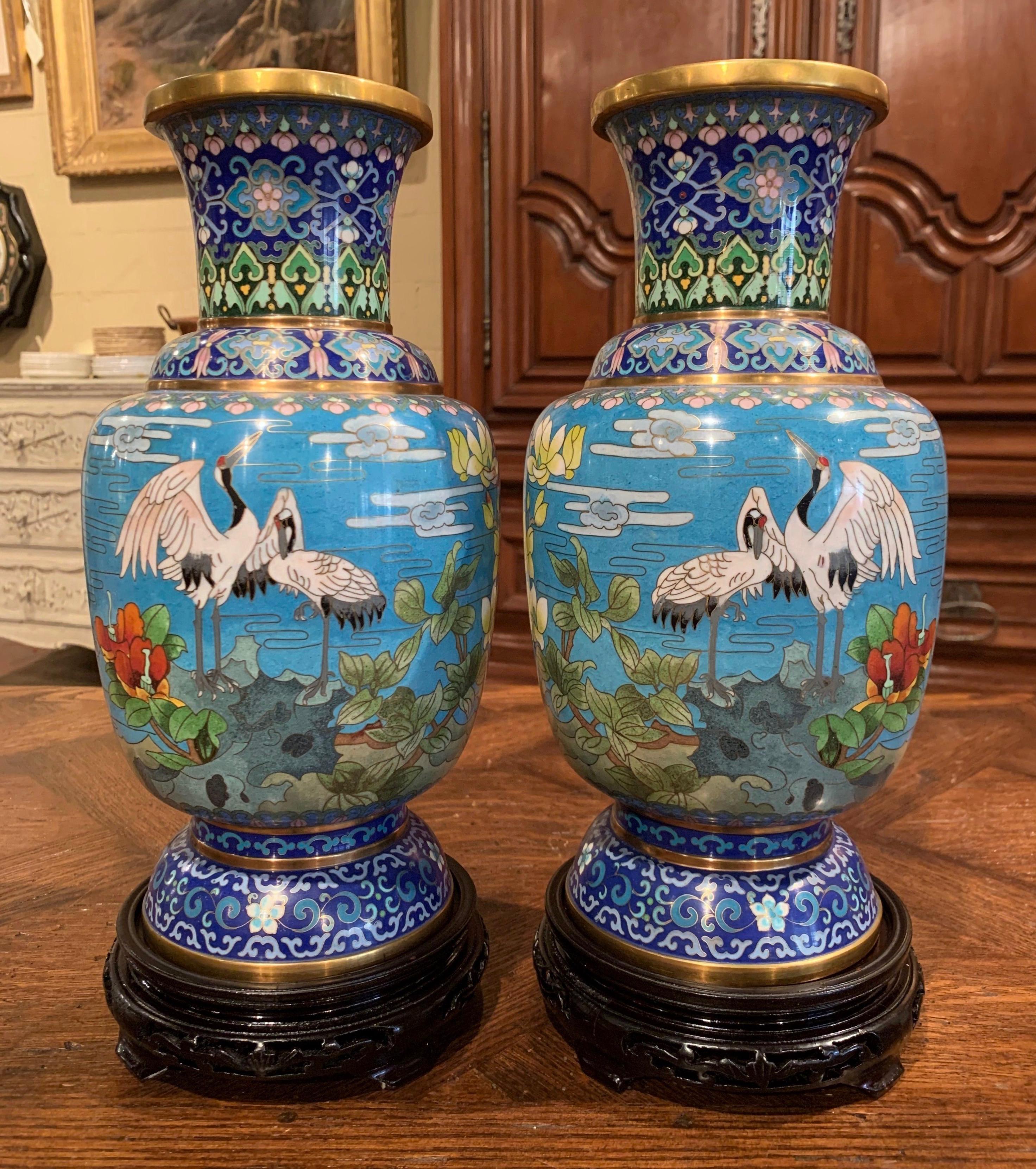 Decorate a mantel with this colorful pair of baluster vases; created in China circa 1960, each vase sits on a carved ebonized wood stand and features floral and bird motifs in rocky landscape in the cloisonné technique (decorative work in which