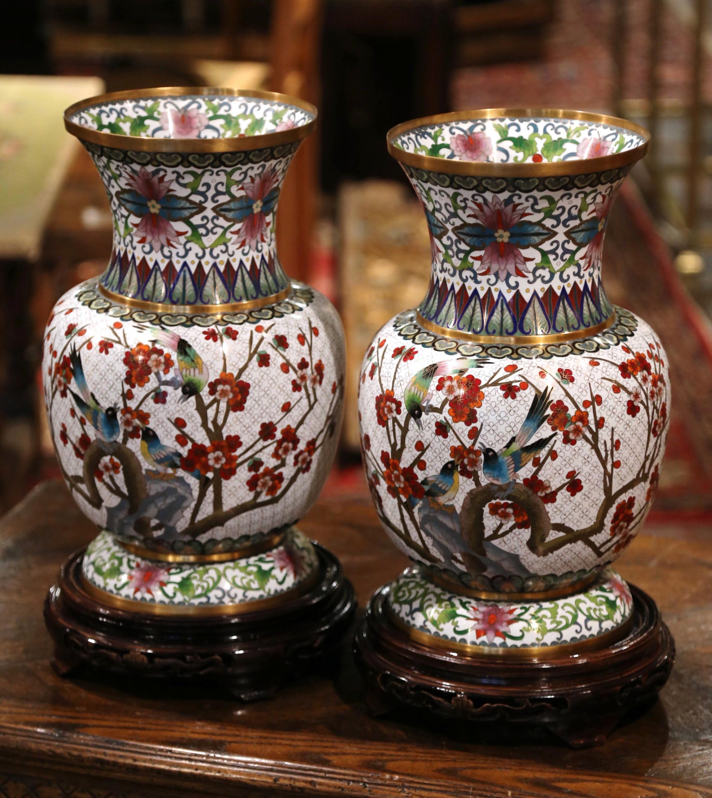 Decorate a mantel with this large pair of champlevé vases, created in China circa 1960, each baluster vase sits on a carved ebonized wood stand and features floral motifs and birds seating on tree branches in the cloisonné technique (decorative work