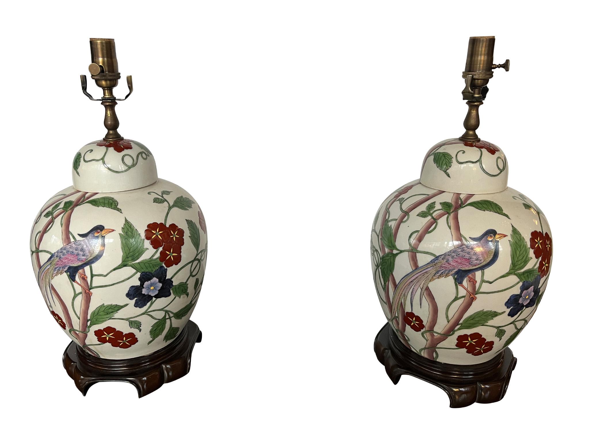 Lovely pair of vintage Chinese table lamps, crafted in porcelain sometime during the 20th century. Designed in a traditional ginger jar shape with a tall brass finial, the lamps feature charming Birds of Paradise and flowering vines decoration. The