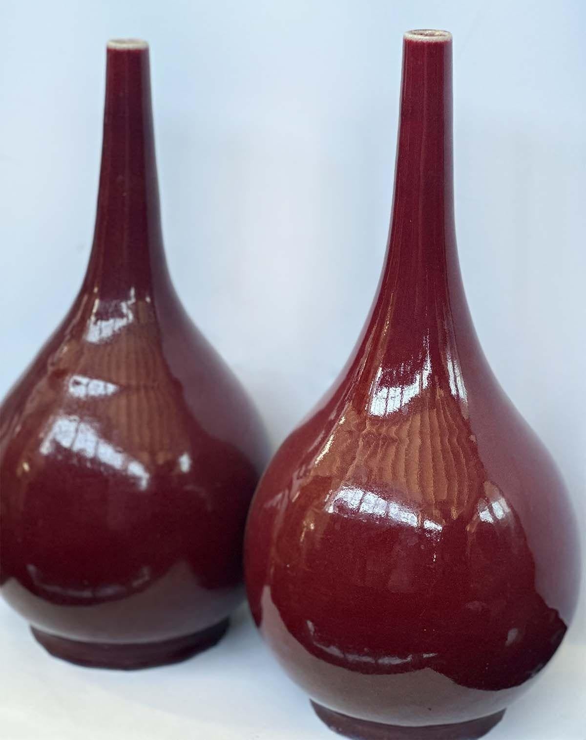 Pair of traditional 20th century Sang de Boeuf vases. Crafted from fine earthenware, each vase boasts a striking deep red glaze, reminiscent of the rich and lustrous hues of 'Sang de Boeuf' or 'Oxblood' glaze, which originated from Chinese ceramics