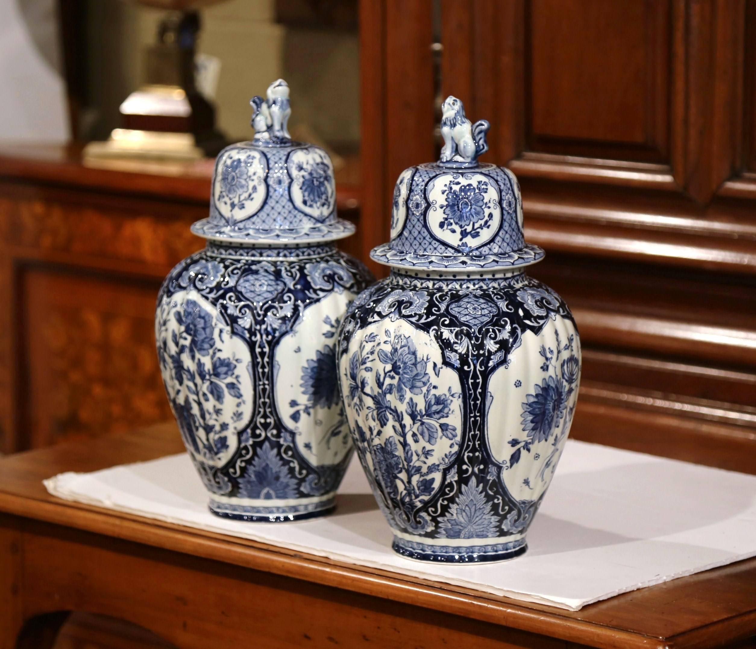 This beautiful pair of vintage ginger jars was crafted in Holland, circa 1920. The ceramic potiches feature hand-painted medallions with classic Dutch flowers and foliage. The traditional blue and white jars have a lid with dog at the top, and are
