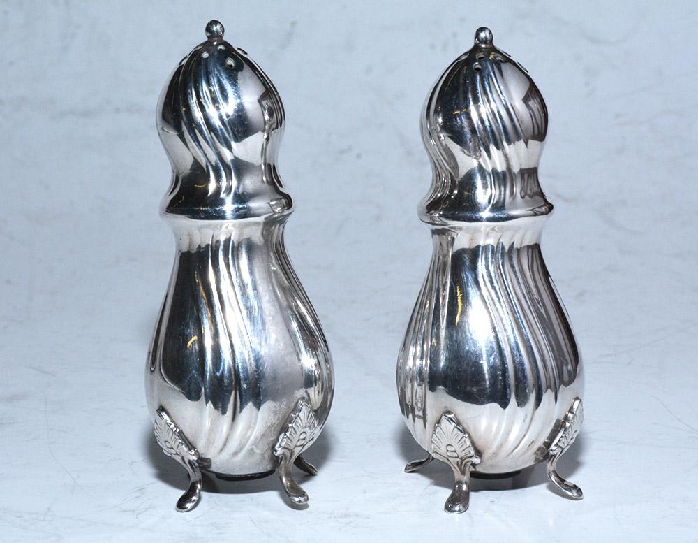Each of the neoclassical pair of 20th century Danish silver plated salt shakers stand on four acanthus-leafed feet. The surfaces are embellished with undulating ribbing. The bottoms have plugged openings. On the bottom of one foot of each Shaker is