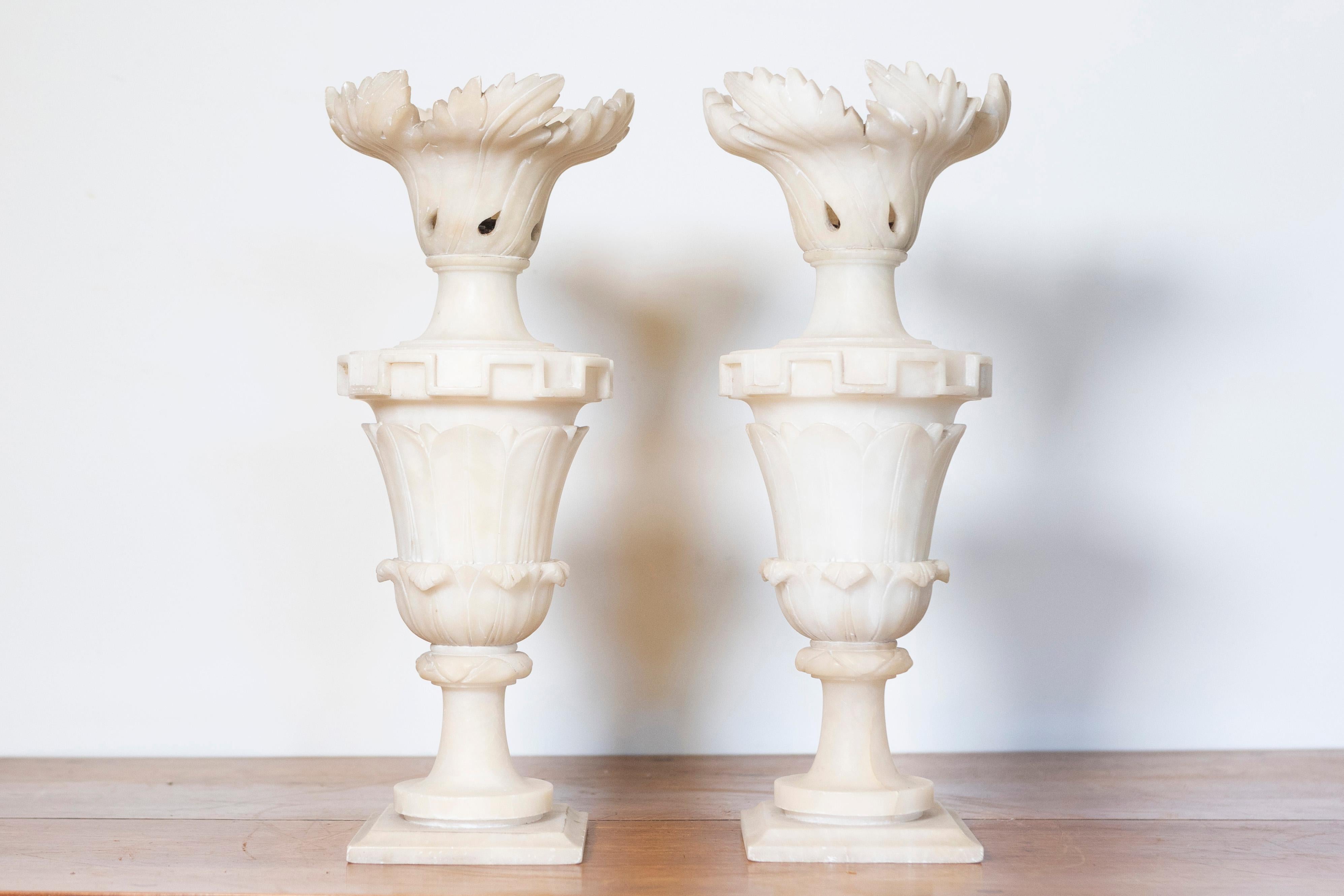 This pair of 20th-century French alabaster elements features intricately designed vases, each with a classical shape and elegant detailing. The vases are crafted from alabaster, showcasing its soft, translucent quality, and the fine craftsmanship is